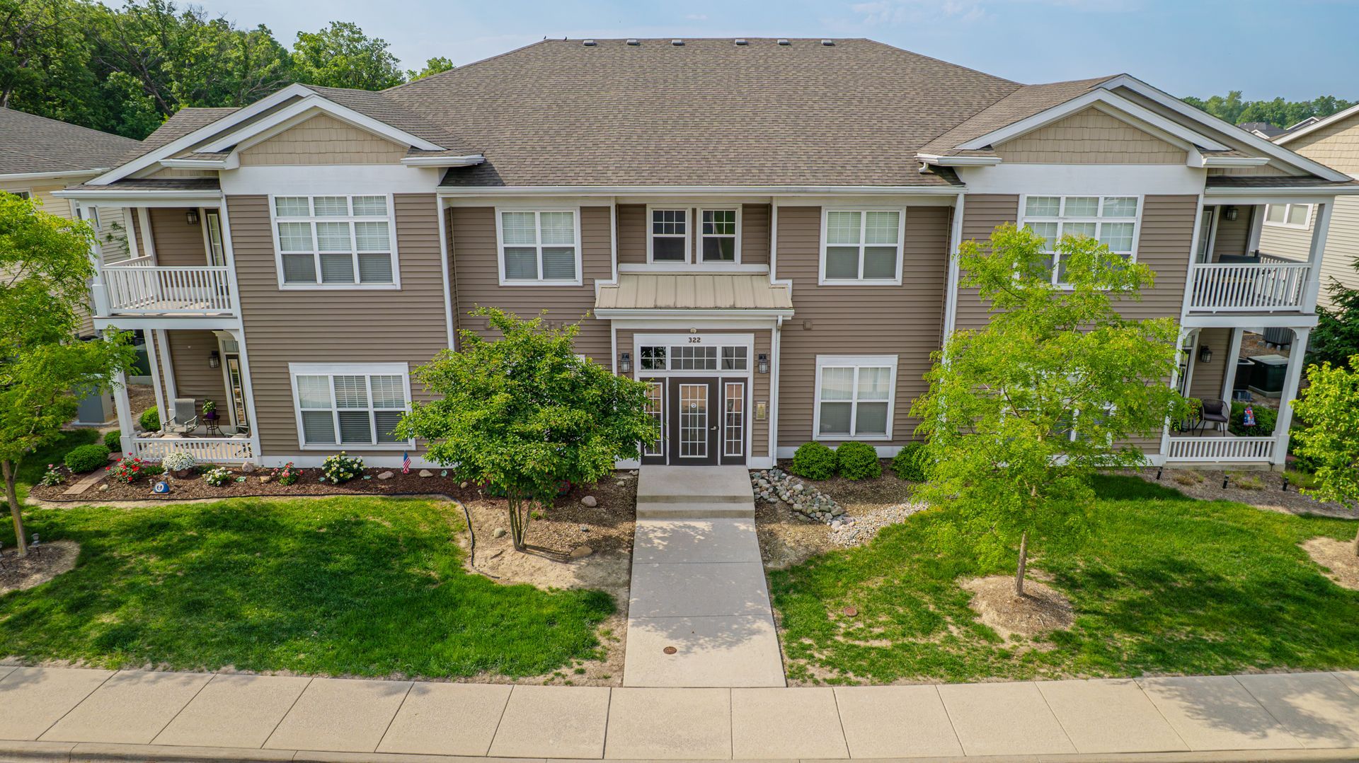 Two-story light yellow apartment building with gray roof, small trees, and green grass lawn.