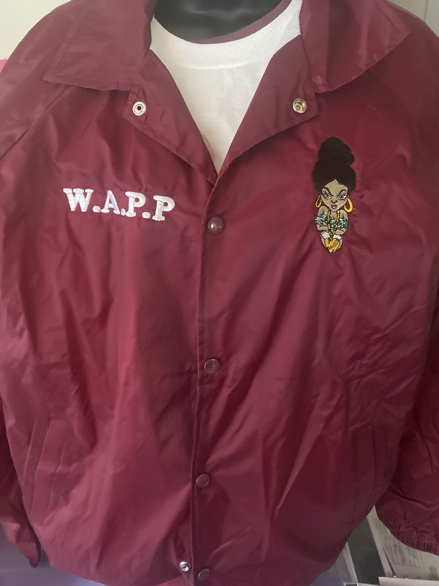 A maroon jacket with a woman embroidered on it is on a mannequin.