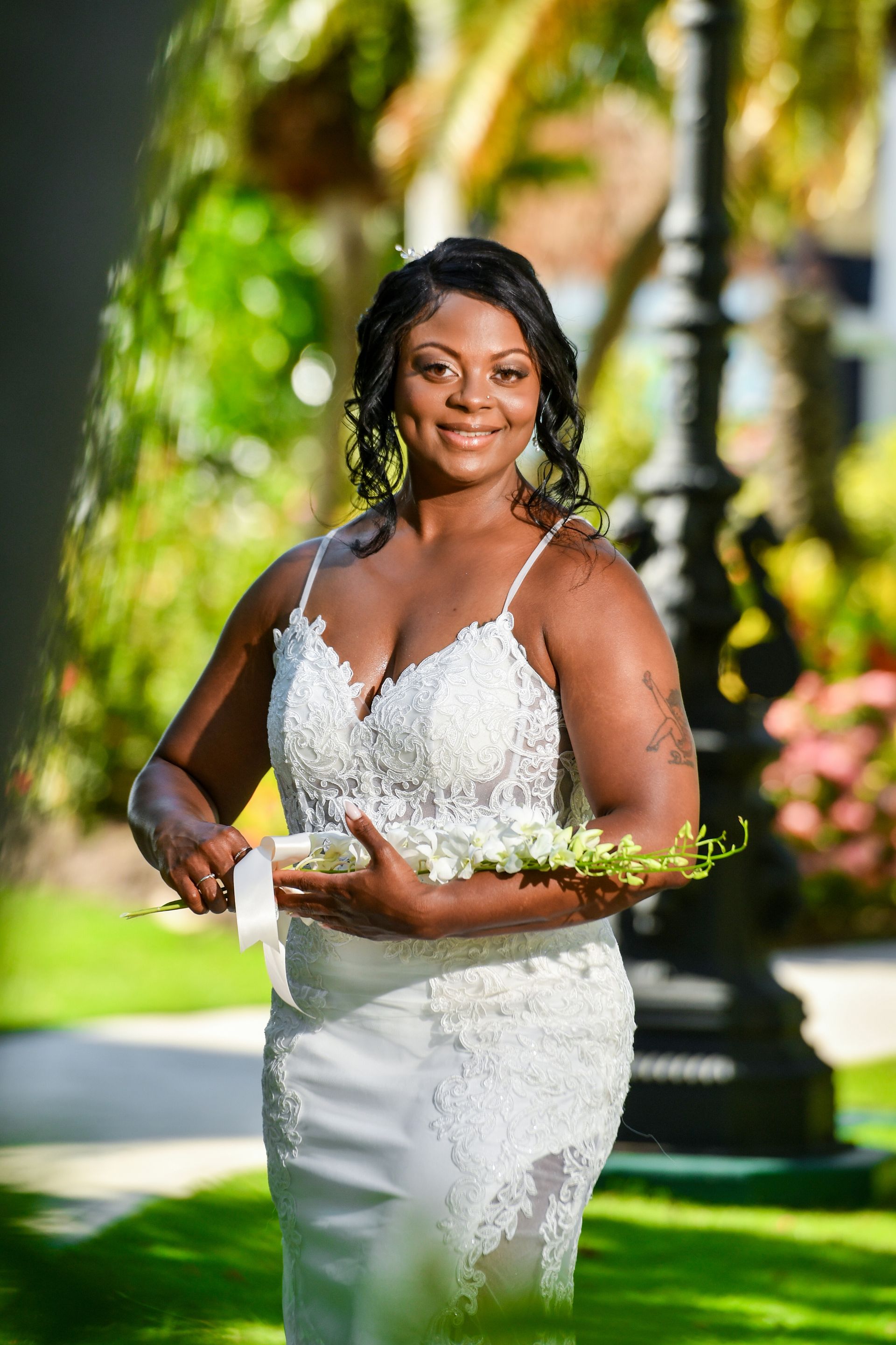Woman in a white beaded dress holding a bouquet outdoors on a sunny lawn