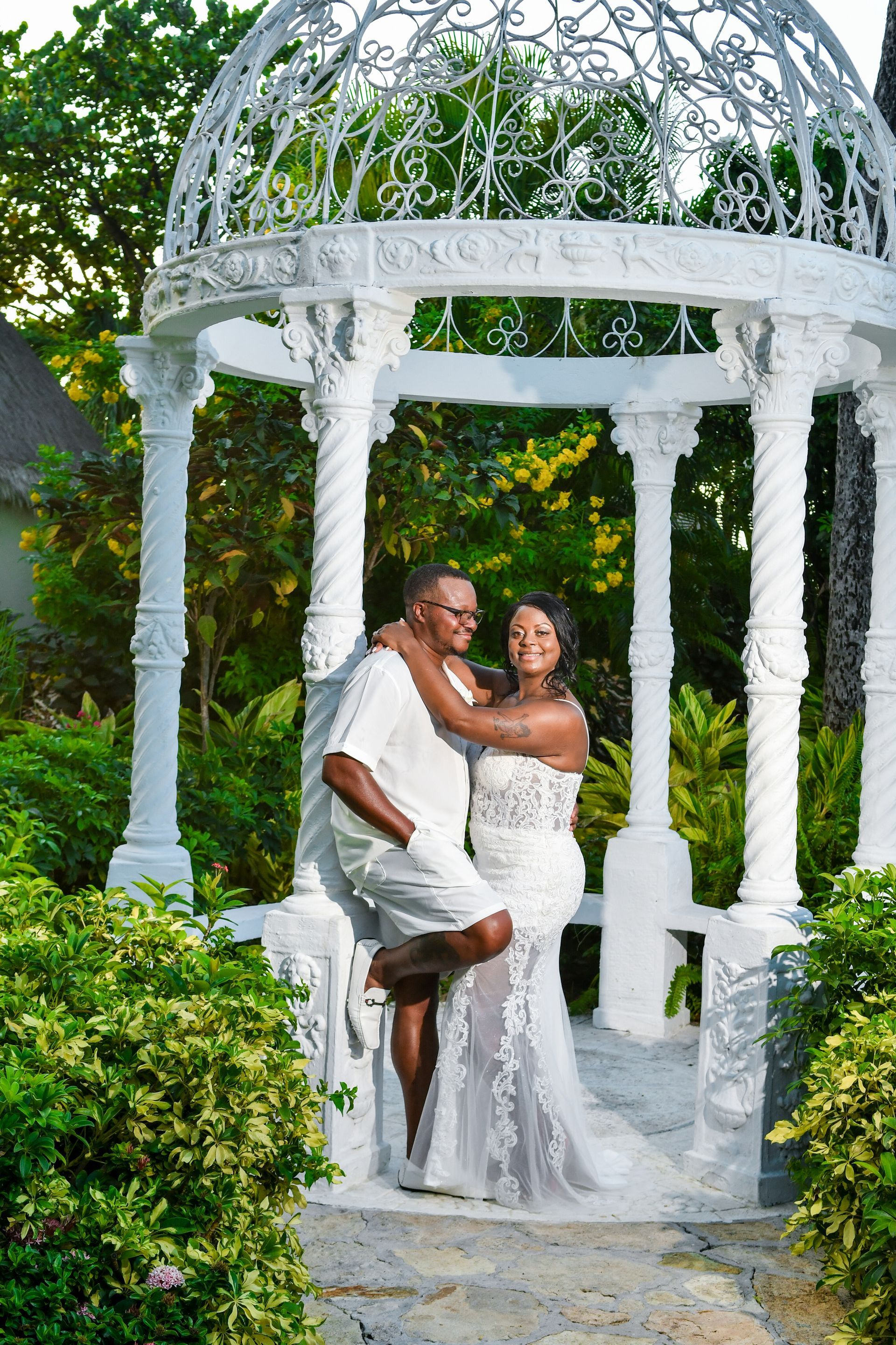 Couple embracing in a white gazebo surrounded by lush greenery.
