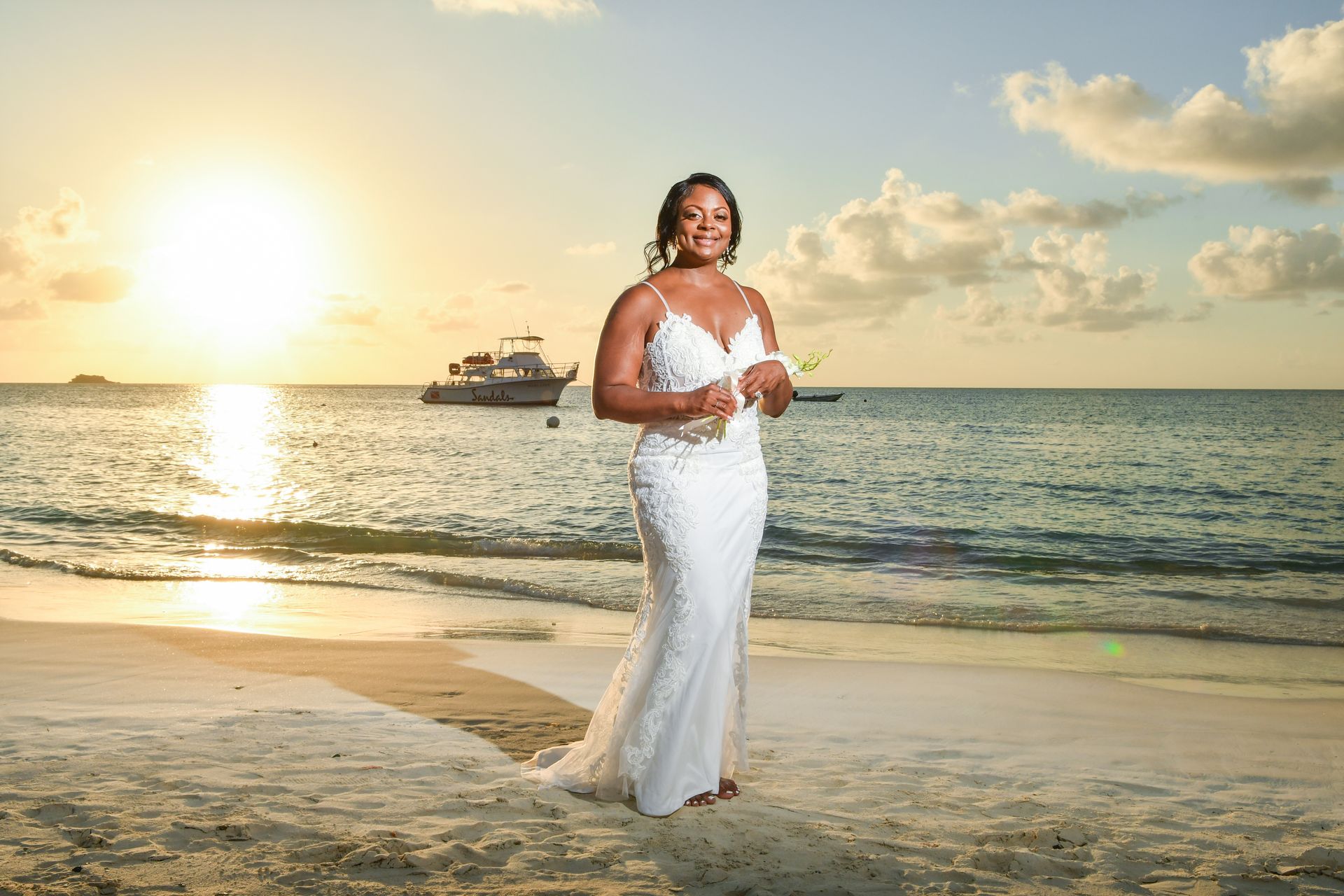 Woman in a white dress standing on a beach at sunset, with a boat on the horizon.