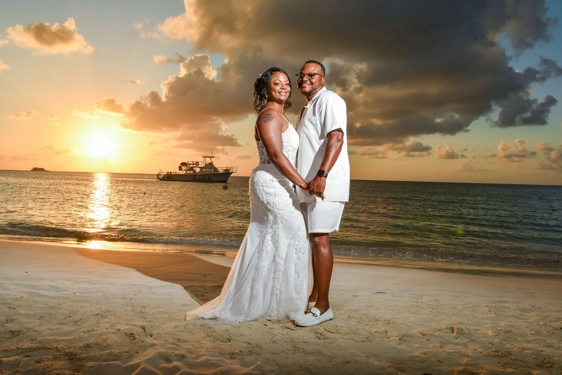 Newlywed couple standing on a beach at sunset, with warm orange light and calm water behind them