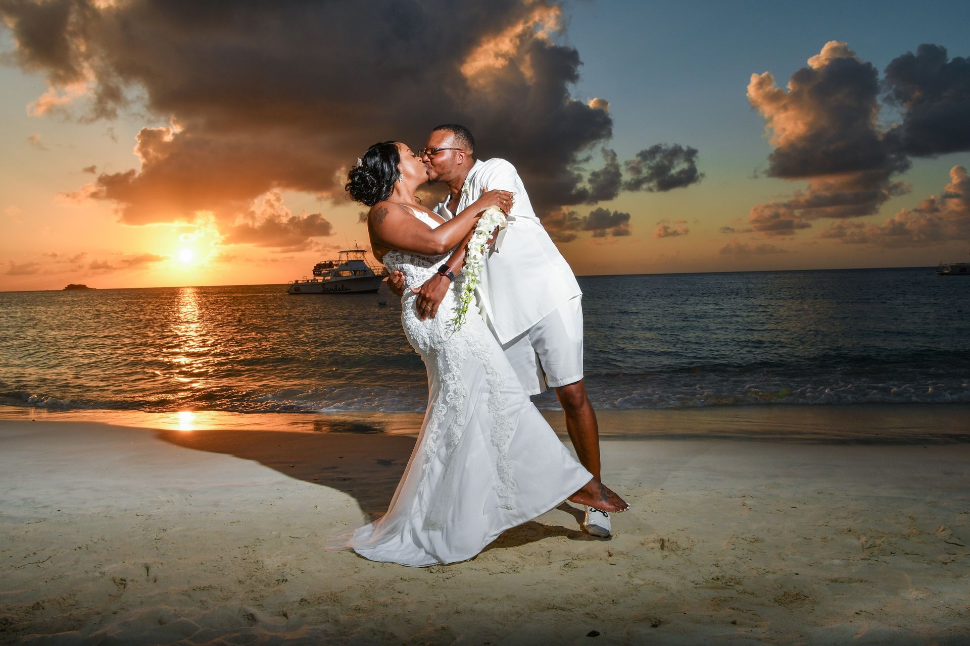 Newlyweds embracing on a beach at sunset with ocean waves and dramatic clouds
