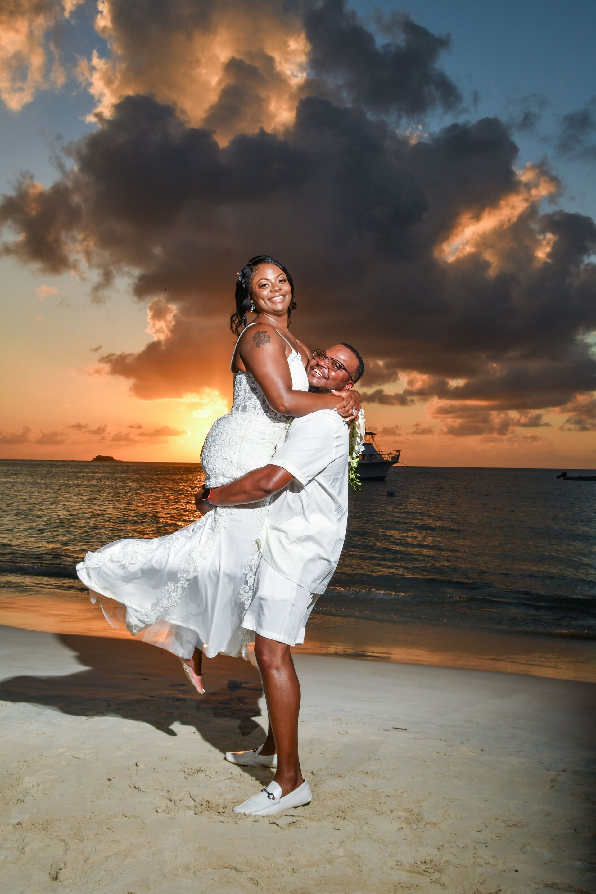 Couple embracing on a beach at sunset, with dramatic clouds and ocean waves behind them