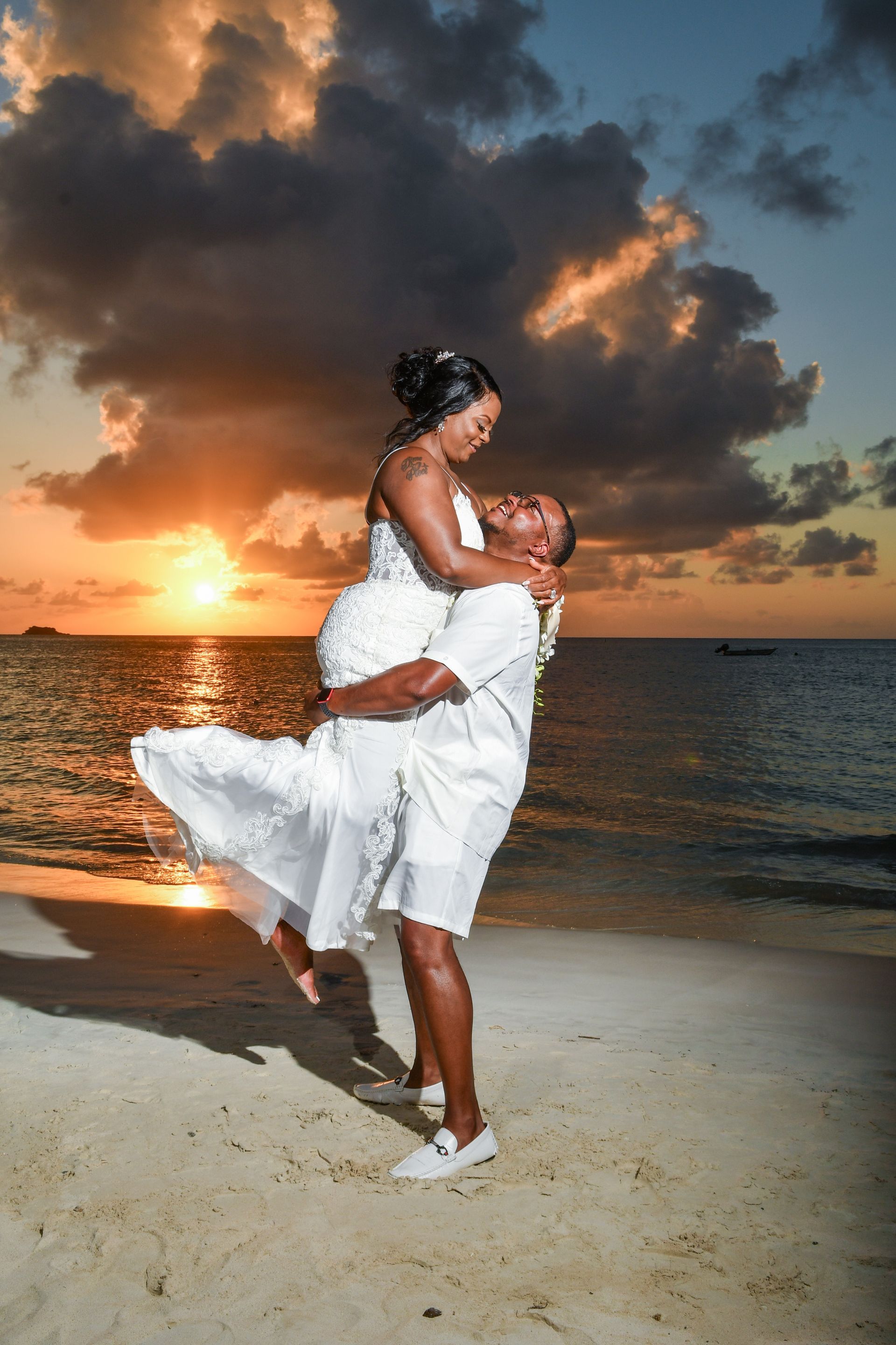 Couple embracing on a beach at sunset, with waves, clouds, and orange sky behind them