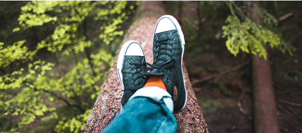 A person 's feet are resting on a tree trunk in the woods.