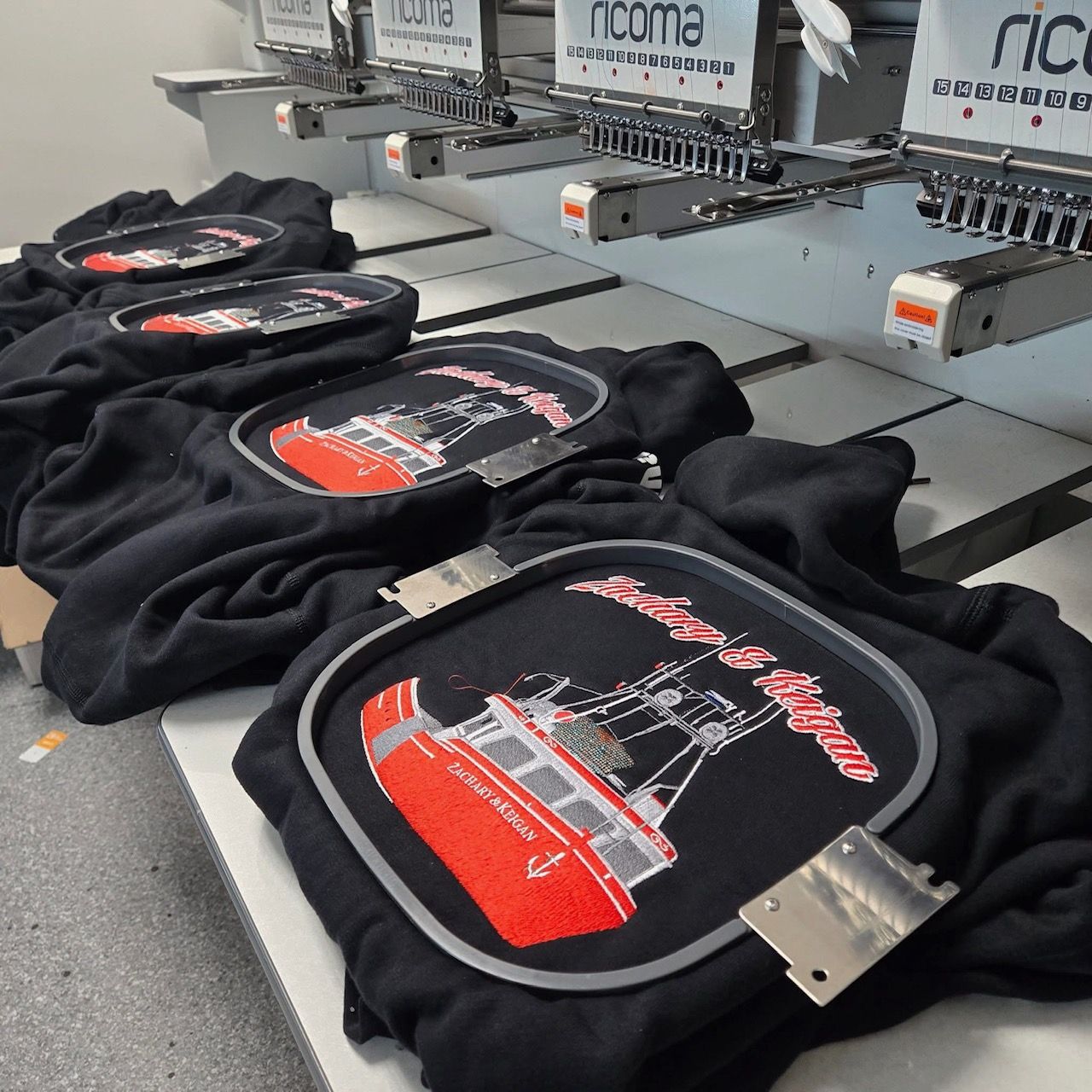 A row of black shirts are being embroidered by ricoma