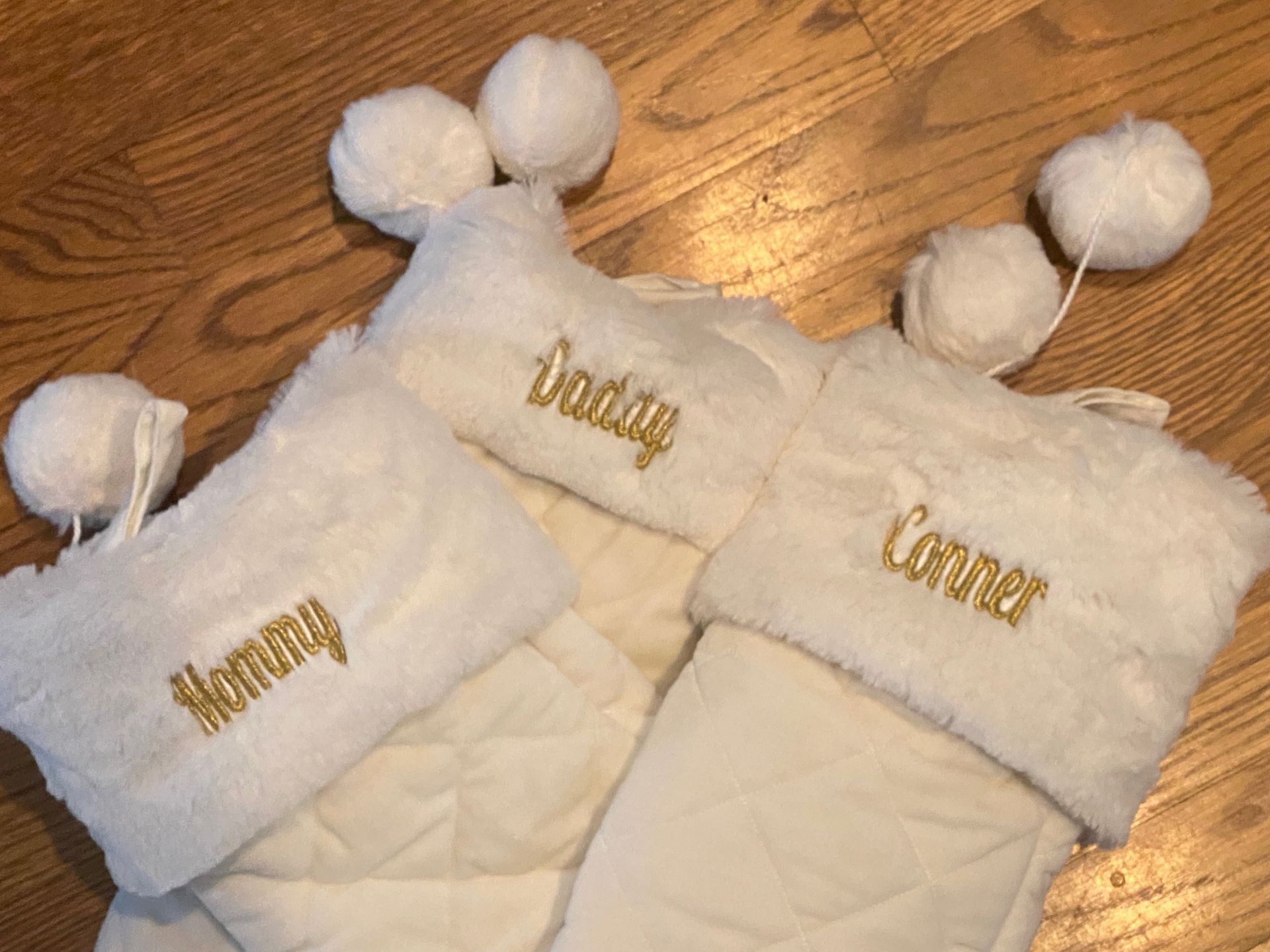 Two white christmas stockings with names on them are sitting on a wooden table.