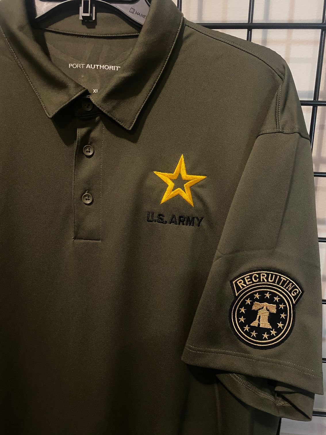 A green u.s. army polo shirt is hanging on a rack.