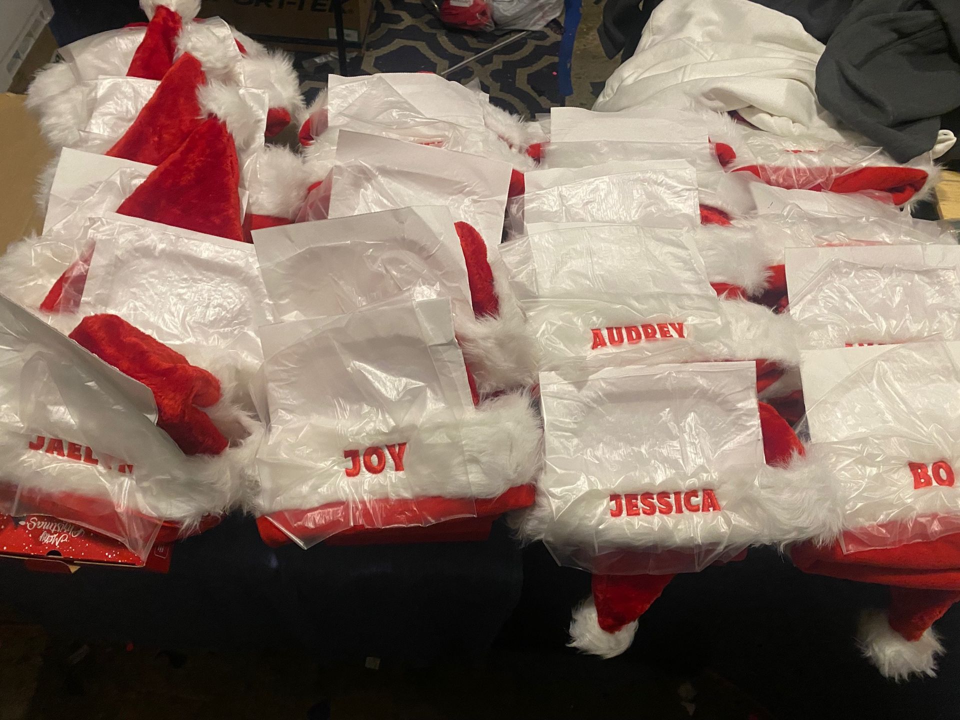 A pile of santa hats with names on them are sitting on a table.
