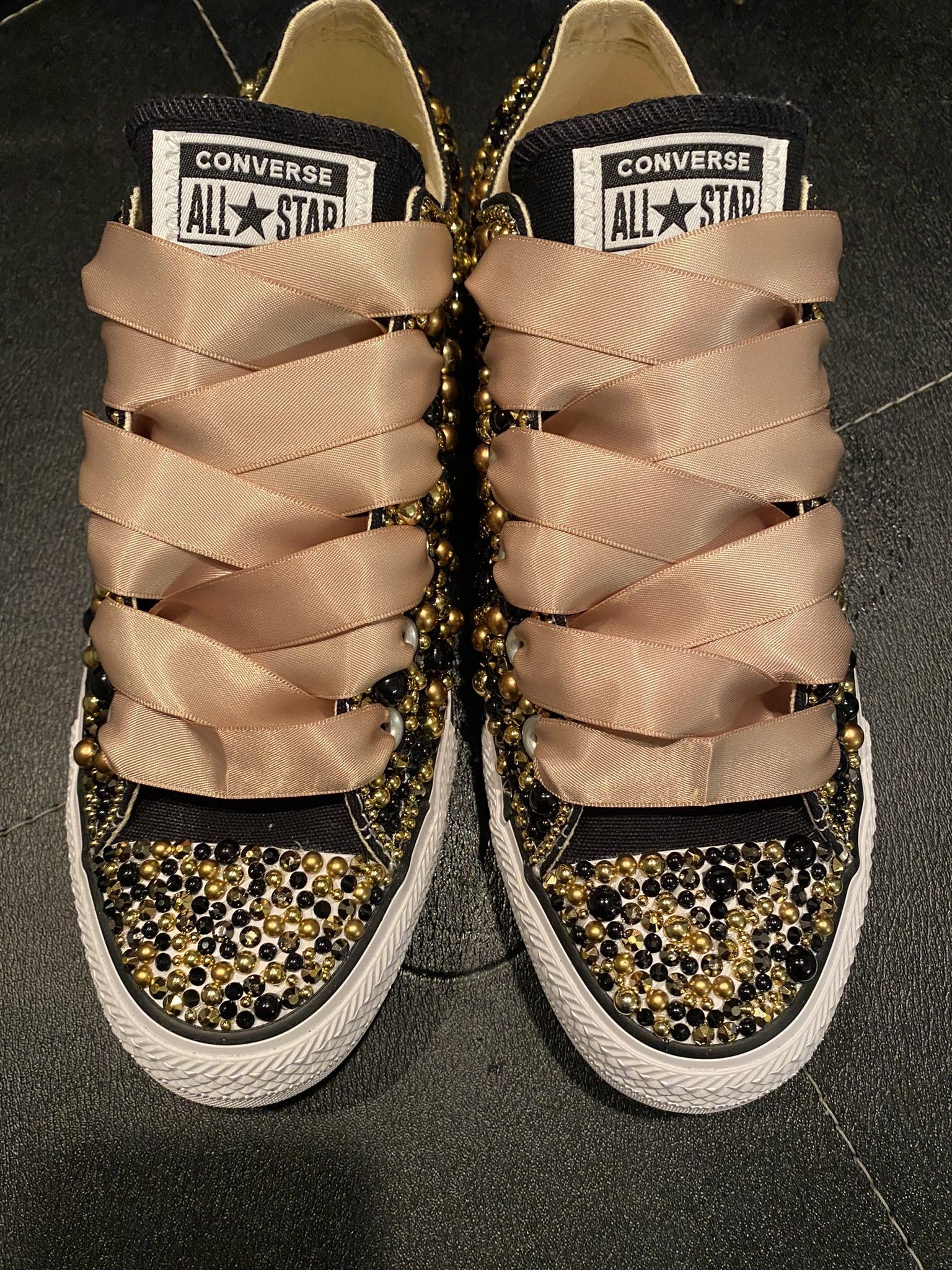 Gold and black Converse sneakers with embellished toe caps and ribbon laces.