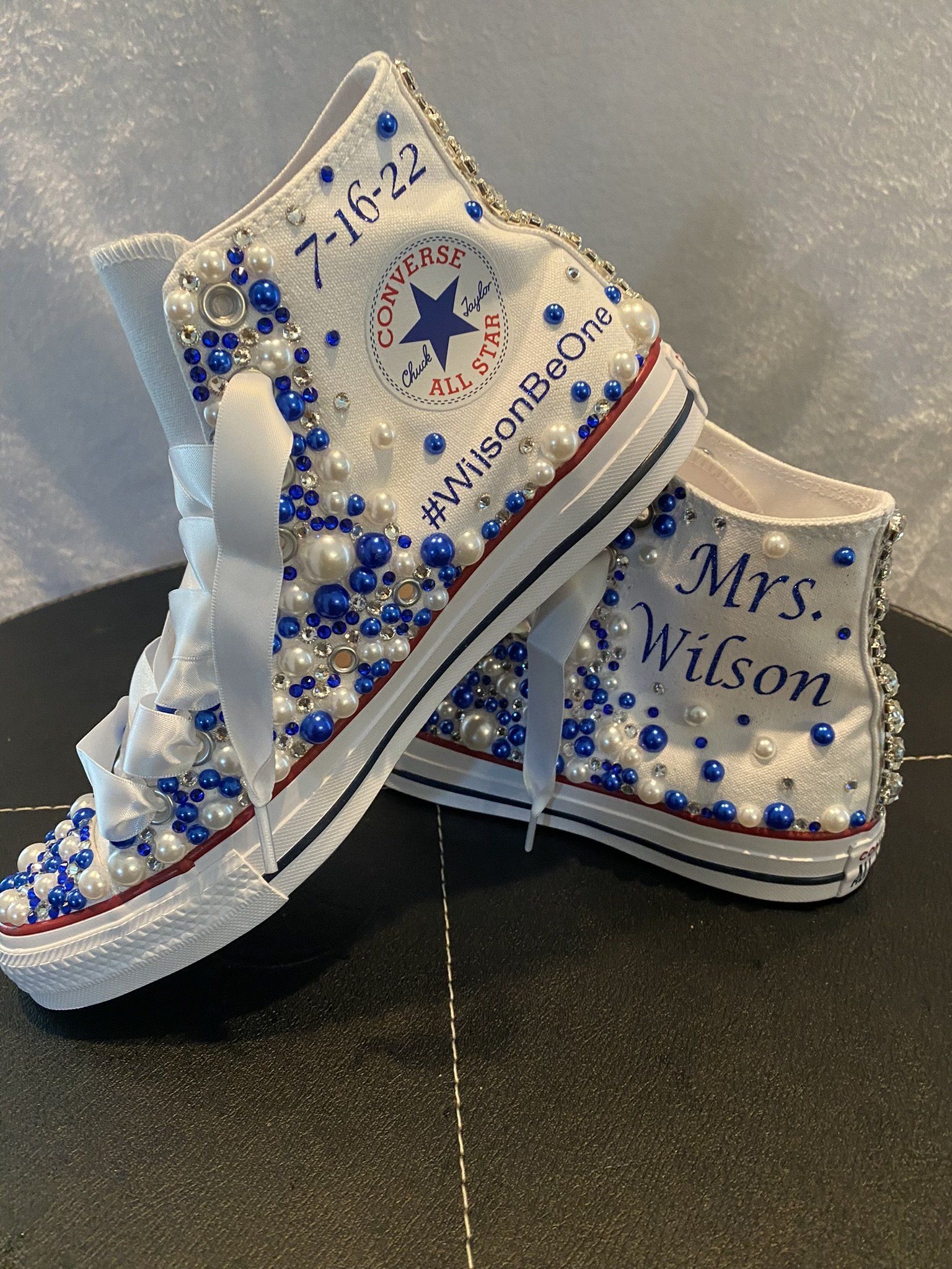 A pair of white converse shoes decorated with blue and white beads and pearls.
