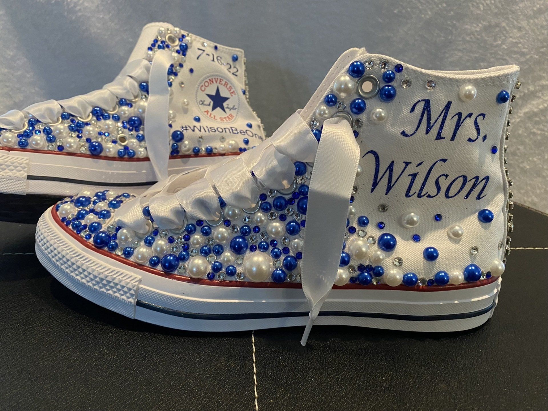 A pair of white converse shoes decorated with blue and white pearls