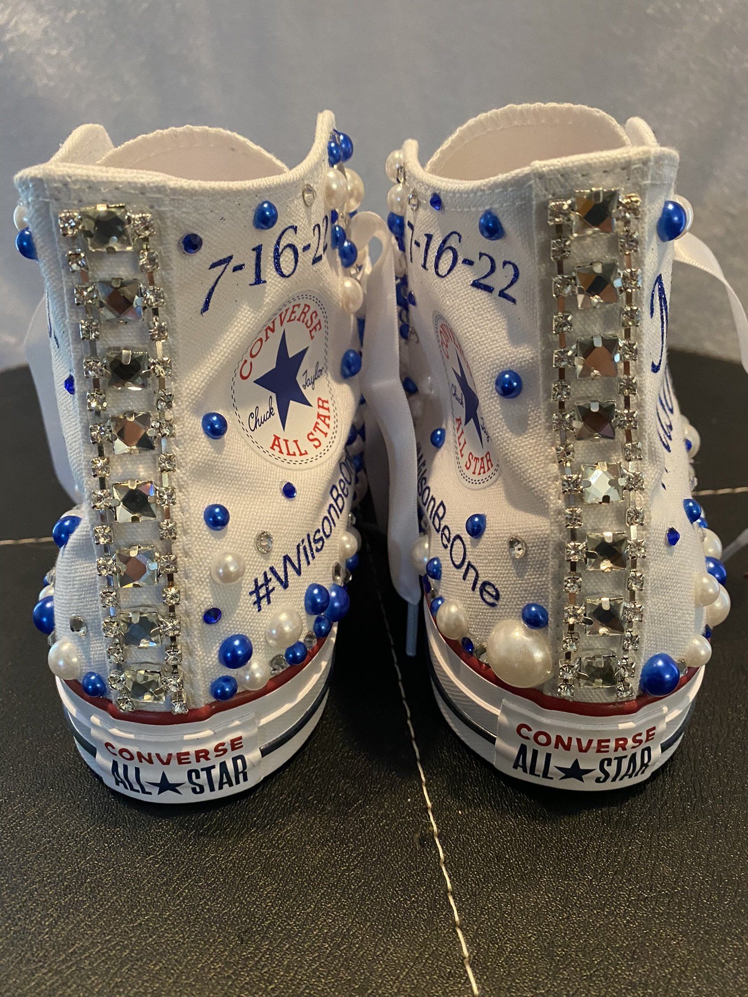 Pair of decorated white Converse sneakers with blue accents and date 