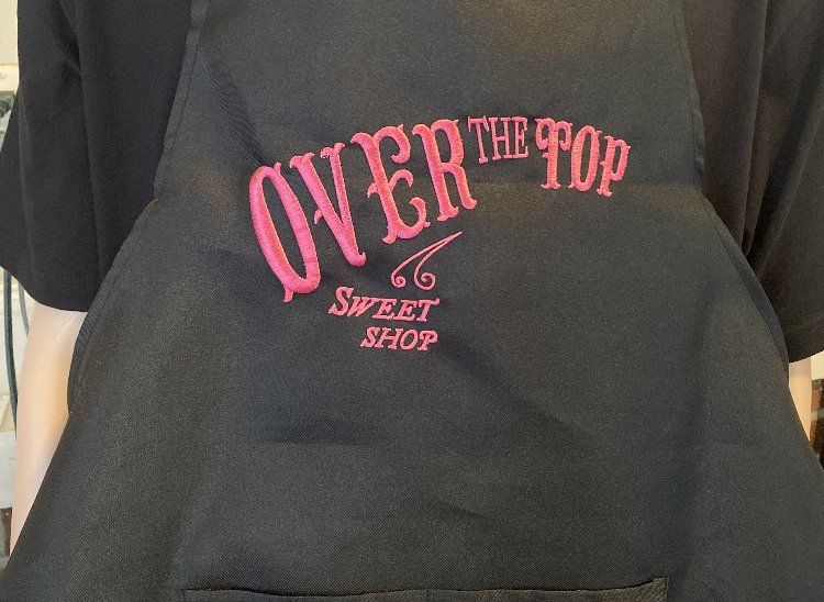 A person wearing an apron that says over the top sweet shop