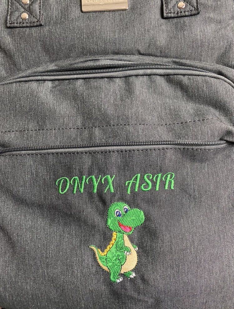 A close up of a backpack with a dinosaur embroidered on it.