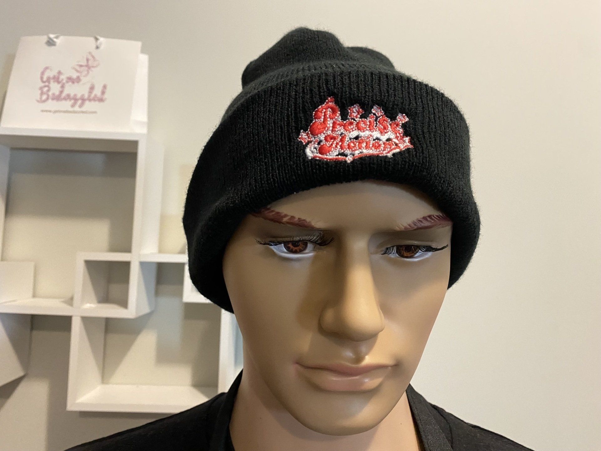 A mannequin wearing a black beanie with a red logo on it