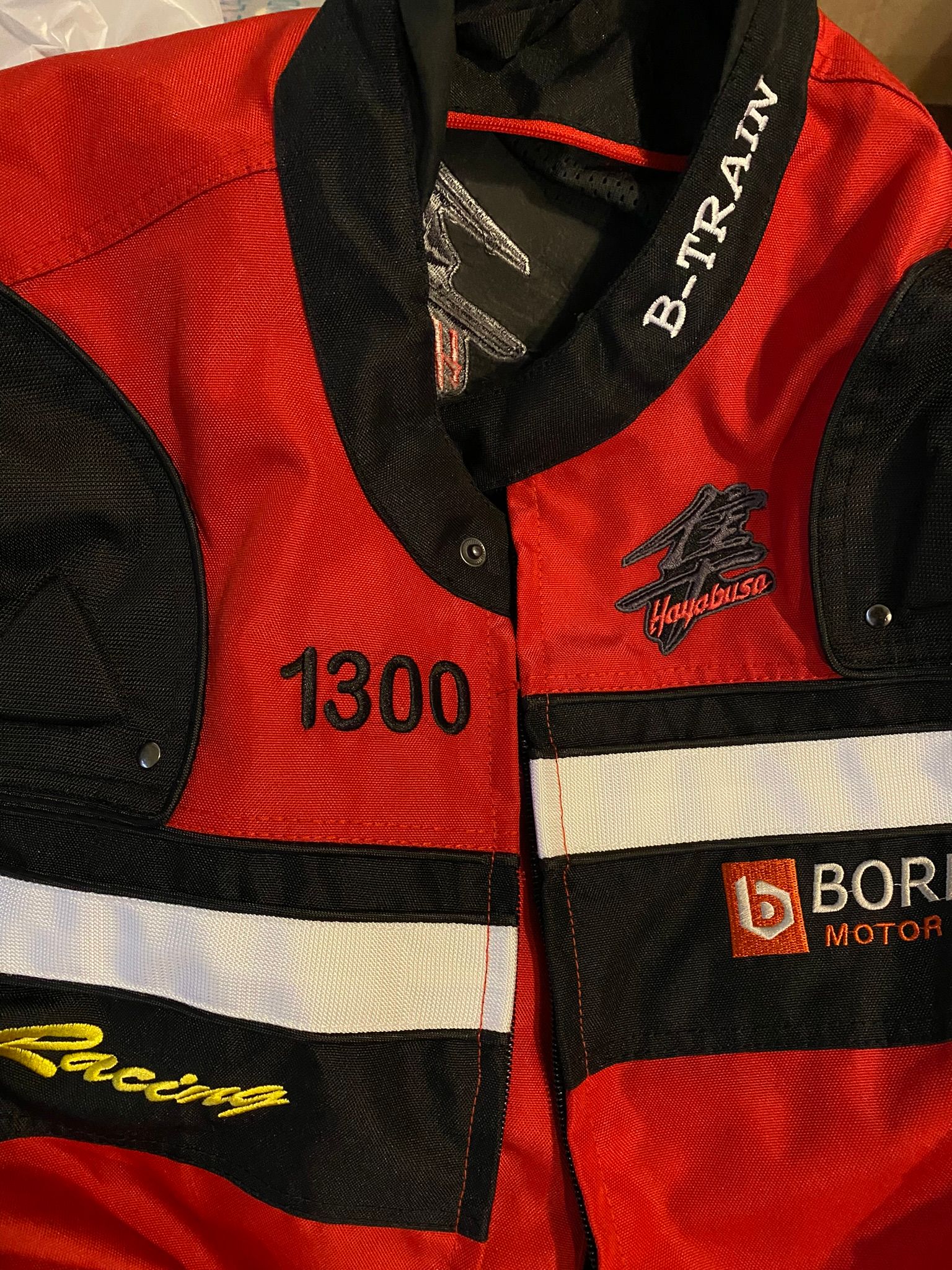A red and black jacket with the number 1300 on it is sitting on a bed.