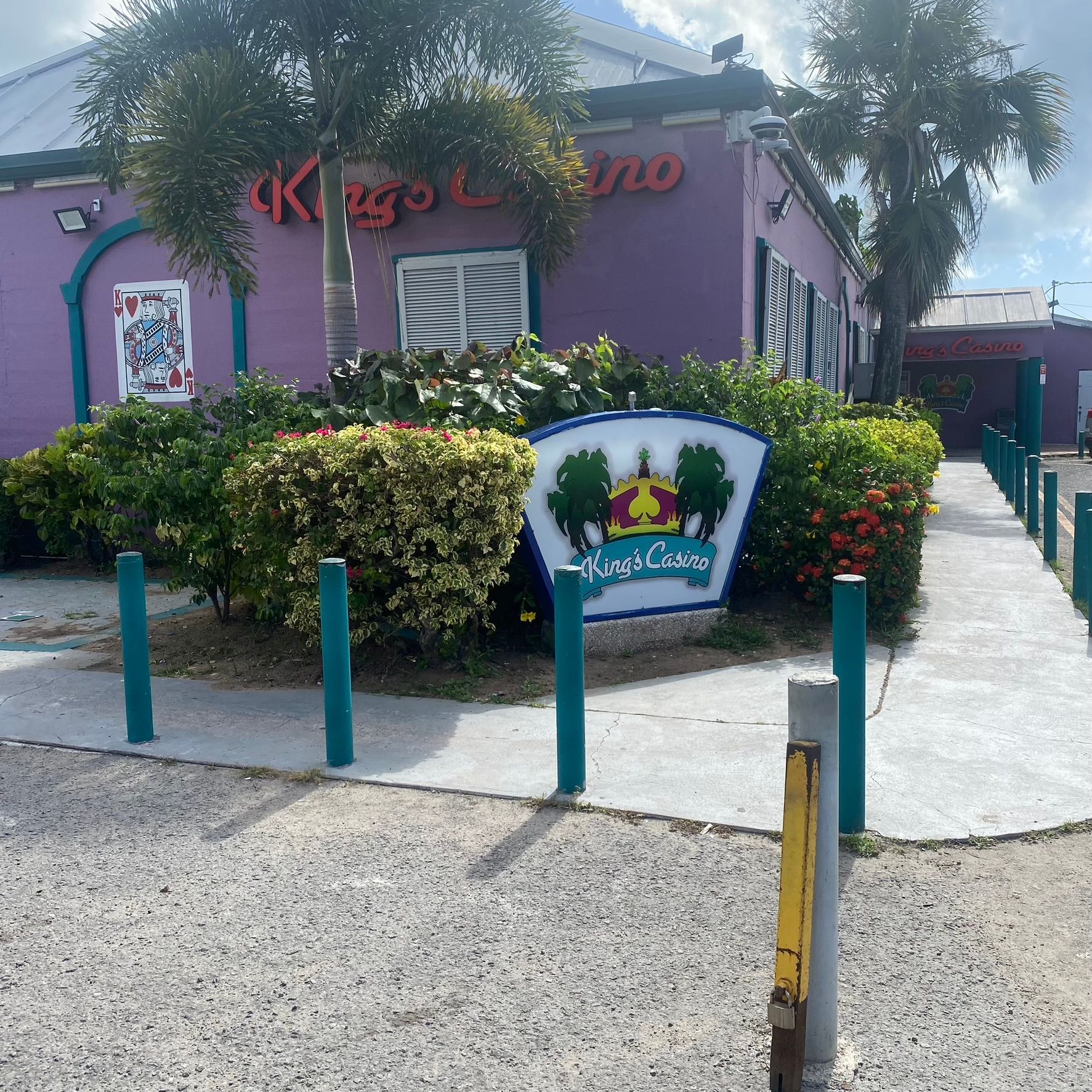 Purple storefront with red sign, hedges, and a walkway beside blue posts and a small sign.