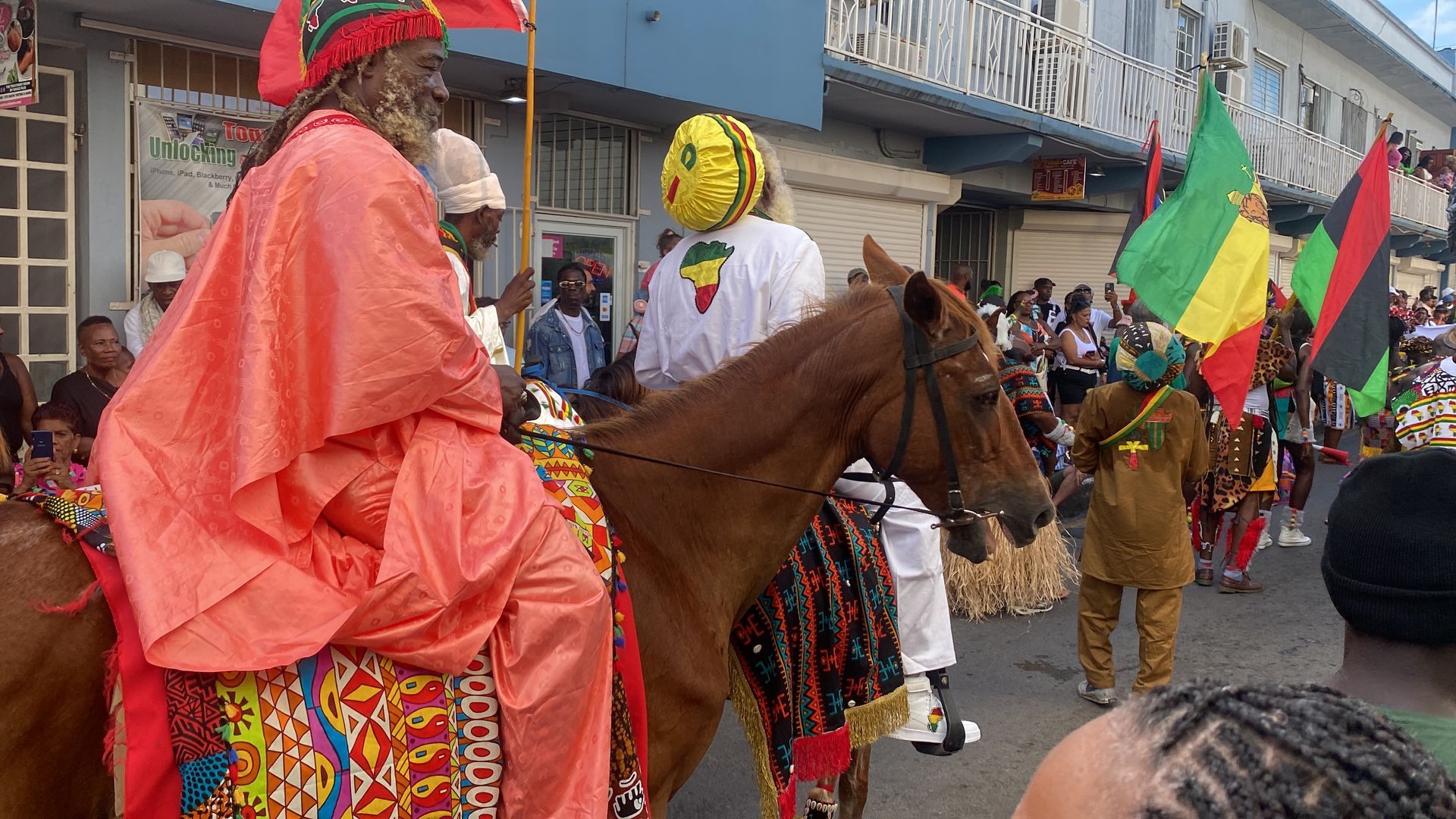 Colorful parade with a rider on a brown horse and participants in bright costumes along a street