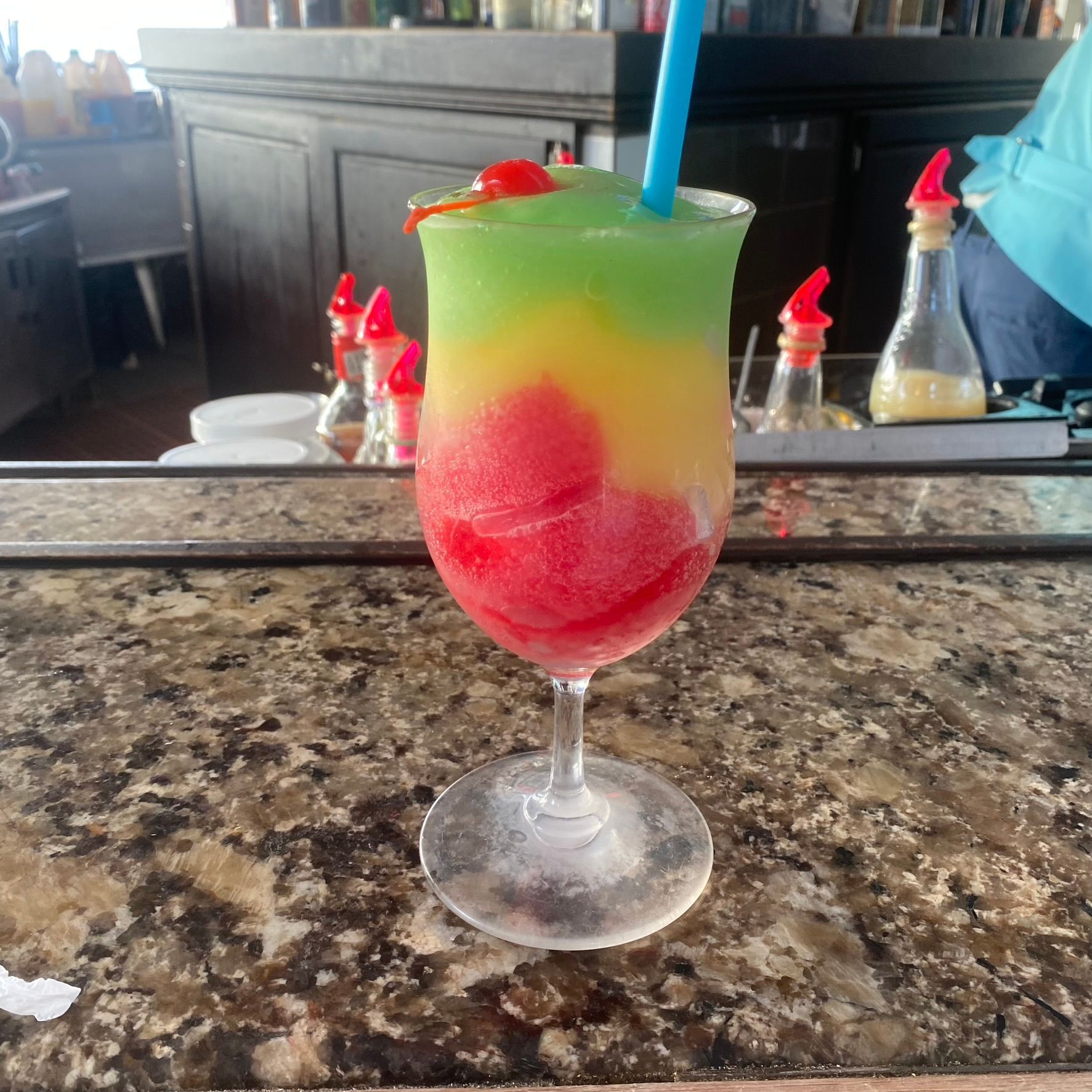 Colorful frozen cocktail in a stemmed glass with a blue straw on a bar counter
