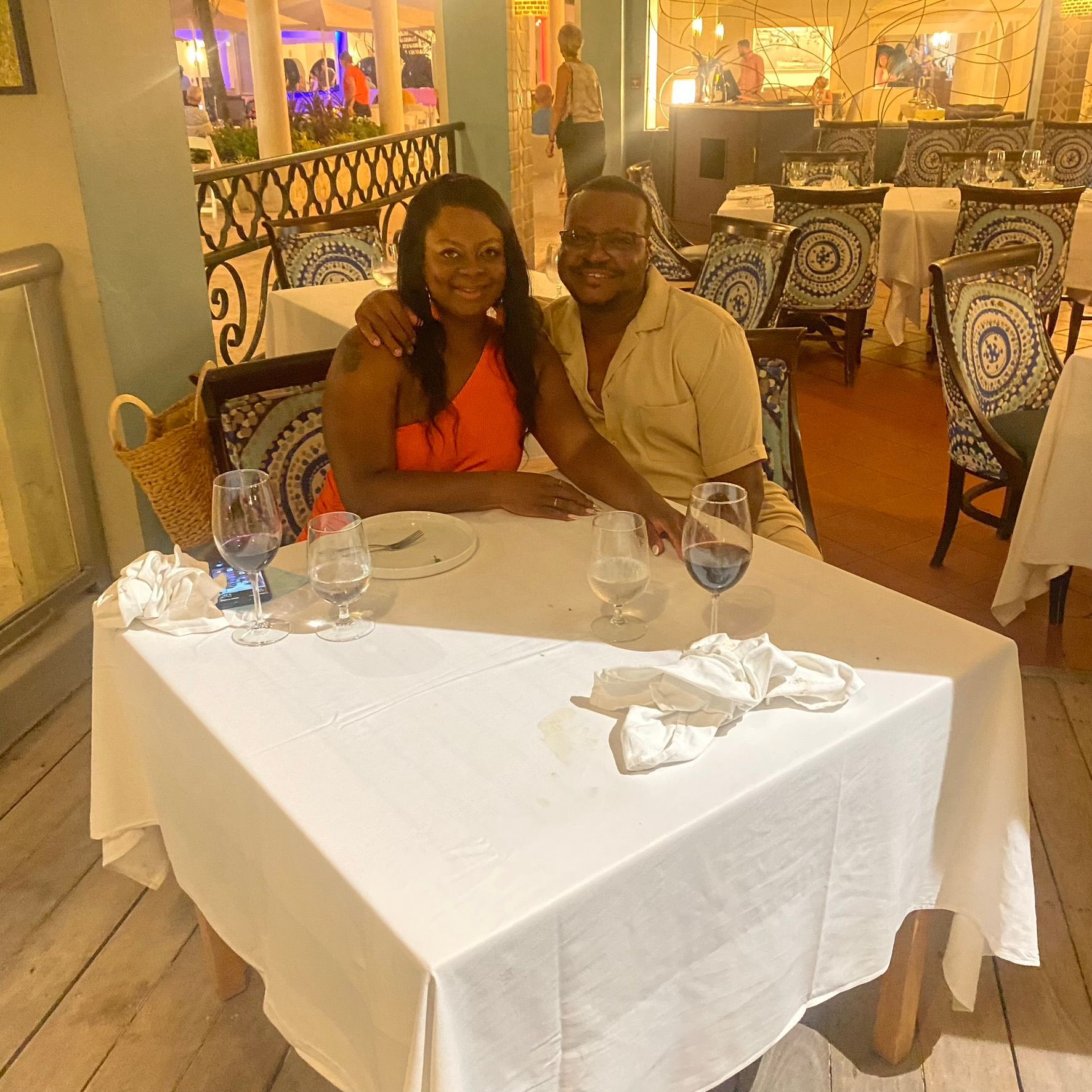 Two people seated at a white-clothed restaurant table, smiling in a warmly lit dining room.