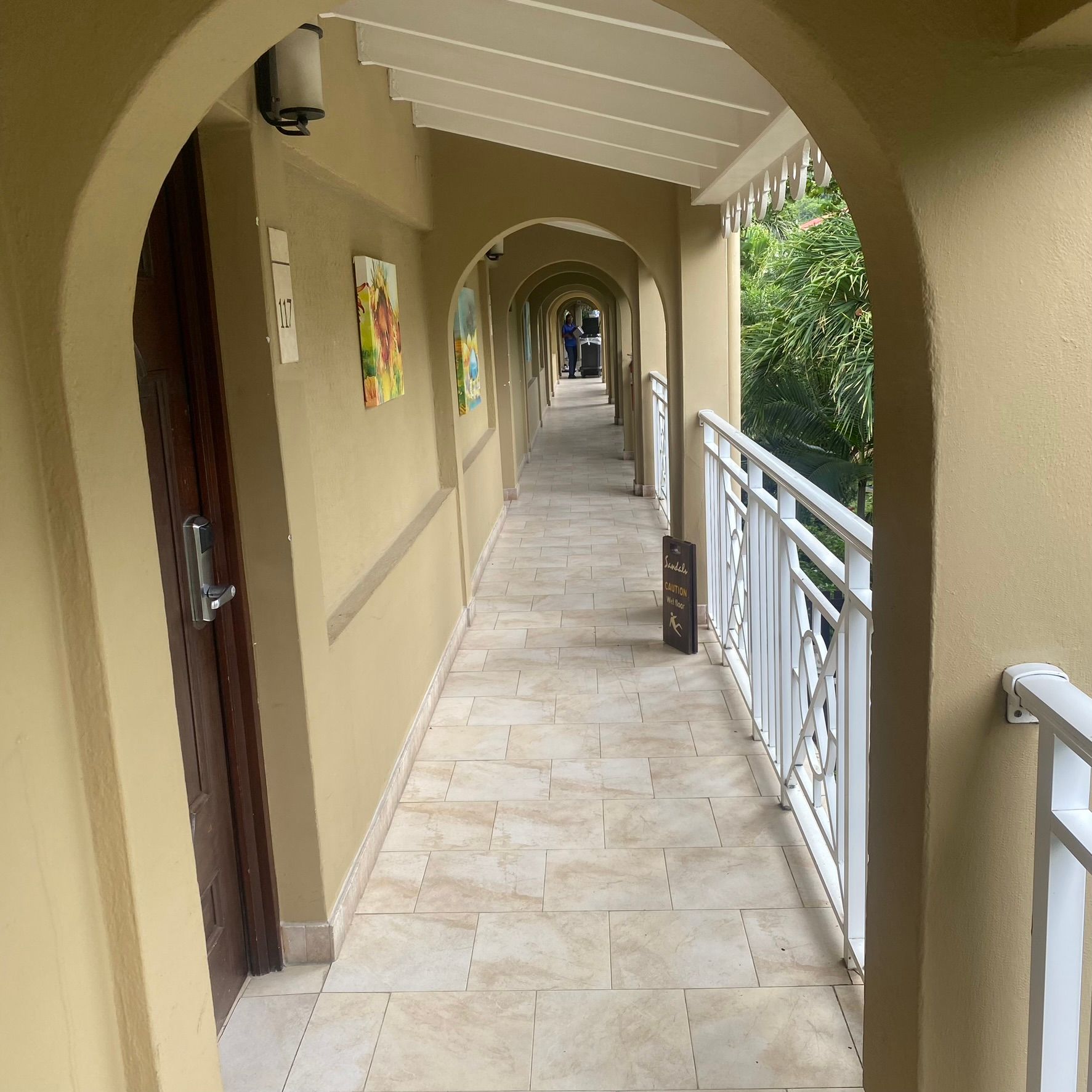 Covered outdoor corridor with beige arches, tiled floor, and white railings overlooking greenery
