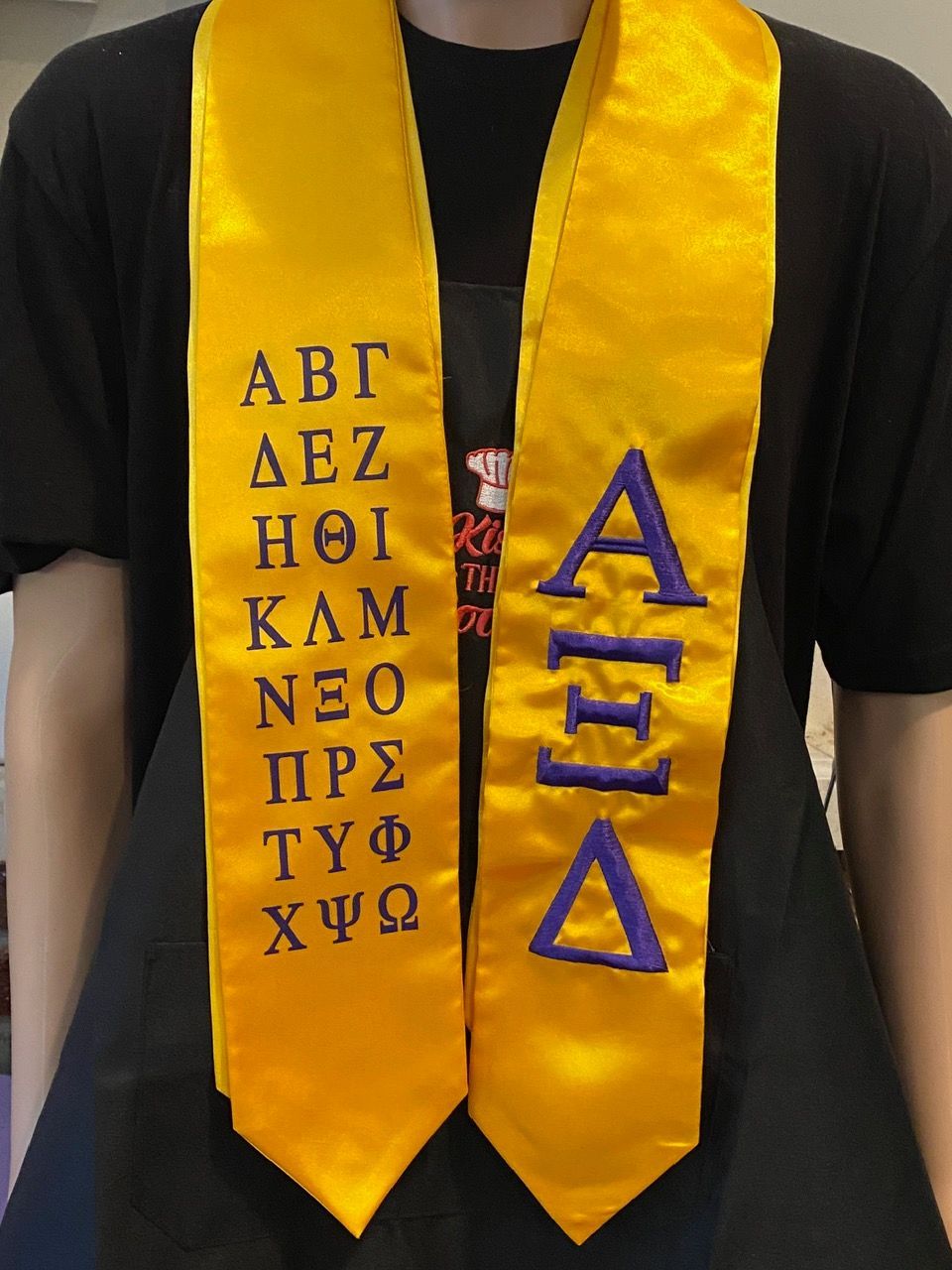 A person is wearing a yellow sash with greek letters on it