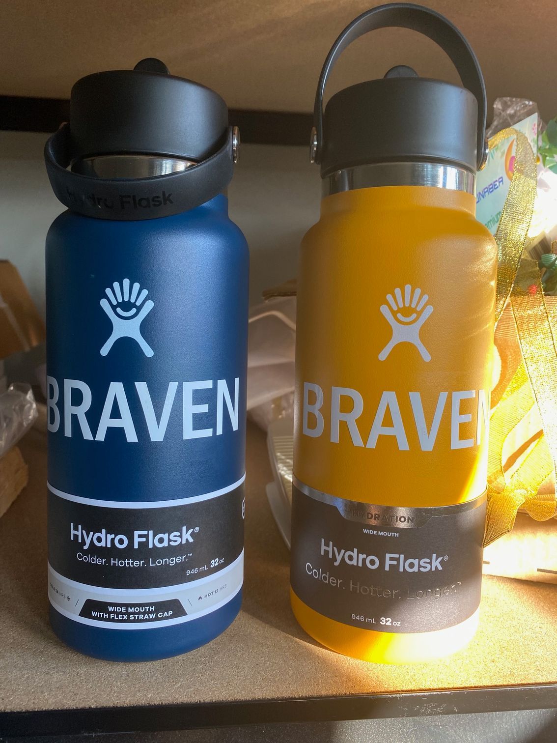 Two hydro flasks , one blue and one yellow , are sitting on a shelf.