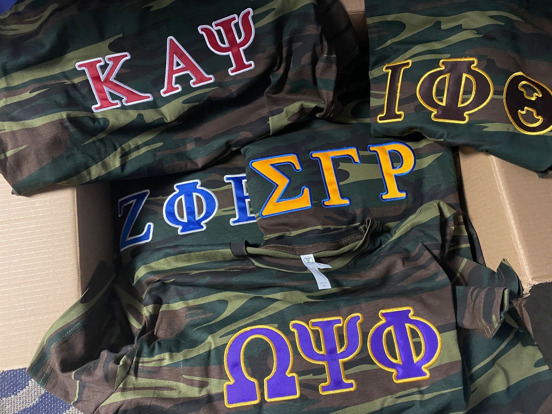 Three camo shirts with greek letters on them