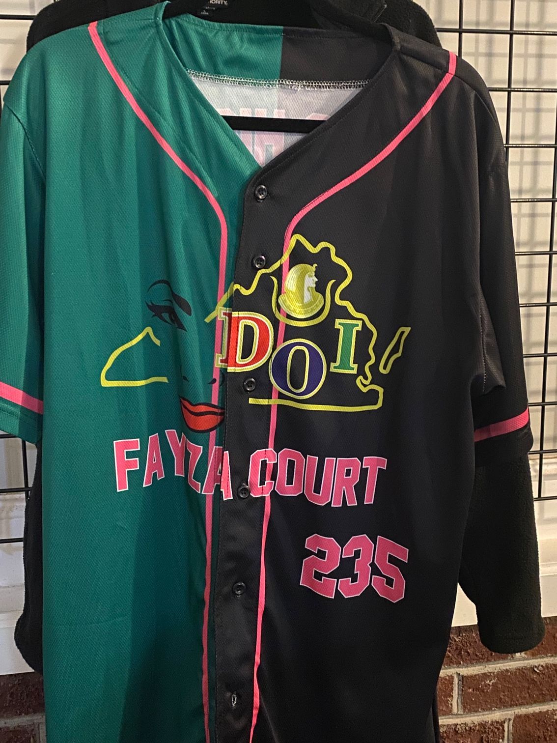 A green and black baseball jersey is hanging on a hanger.