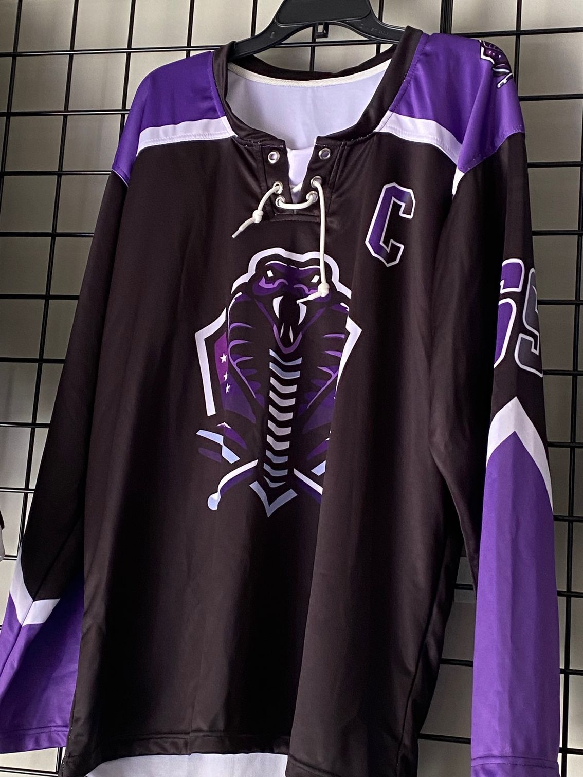 A black and purple hockey jersey is hanging on a hanger.