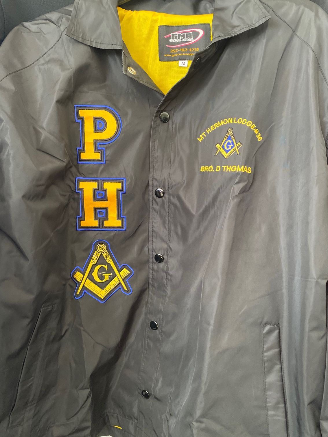 A black jacket with a masonic symbol on it is hanging on a hanger.