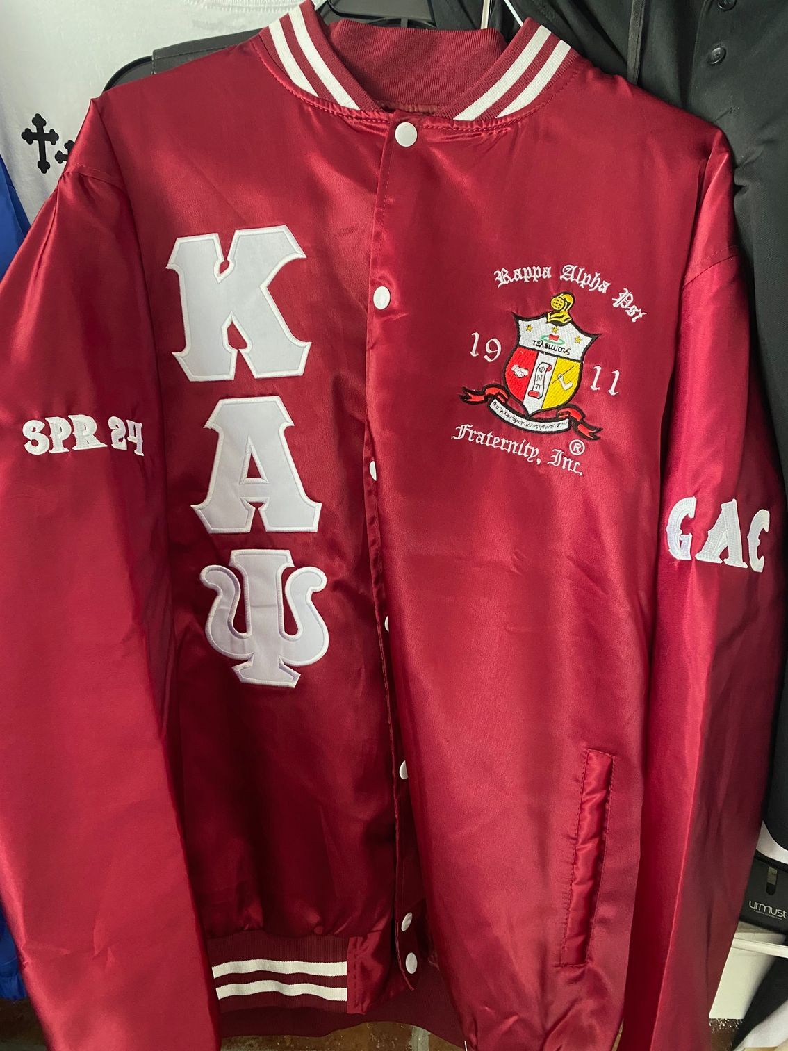 A maroon jacket with white letters on it is hanging on a hanger.