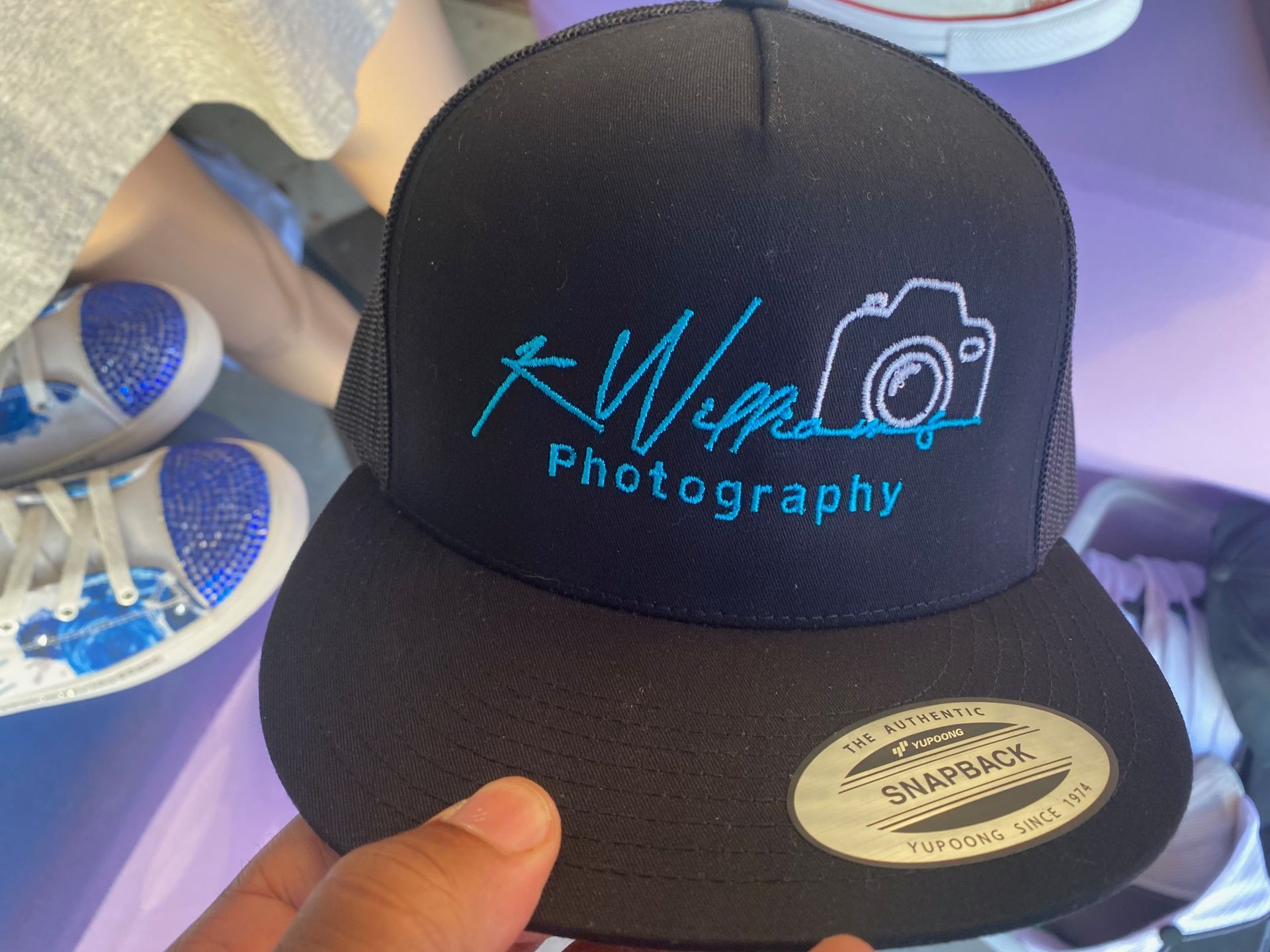 A person is holding a black hat that says photography on it
