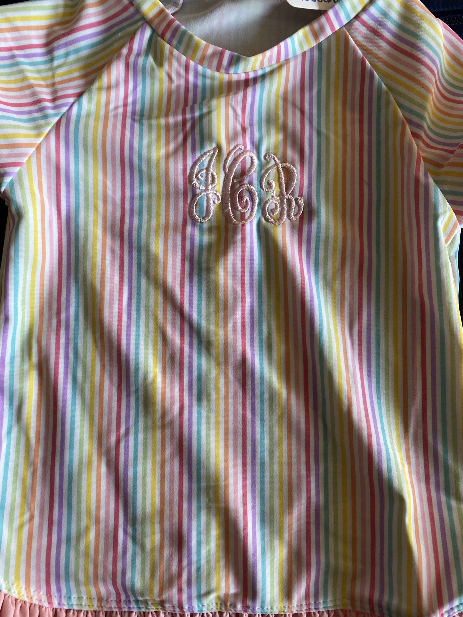 A close up of a rainbow striped shirt with a monogram on it.