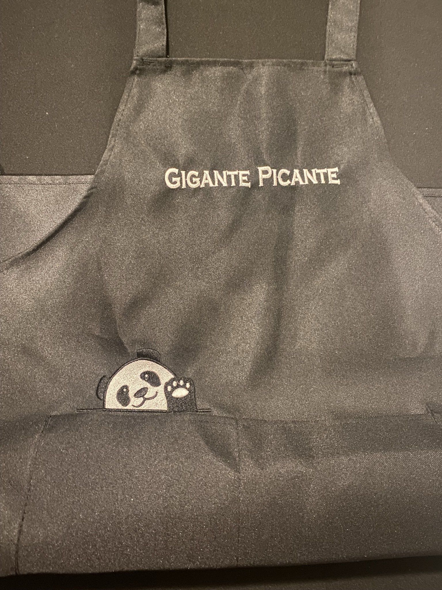 A black apron with the words gigante picante embroidered on it.
