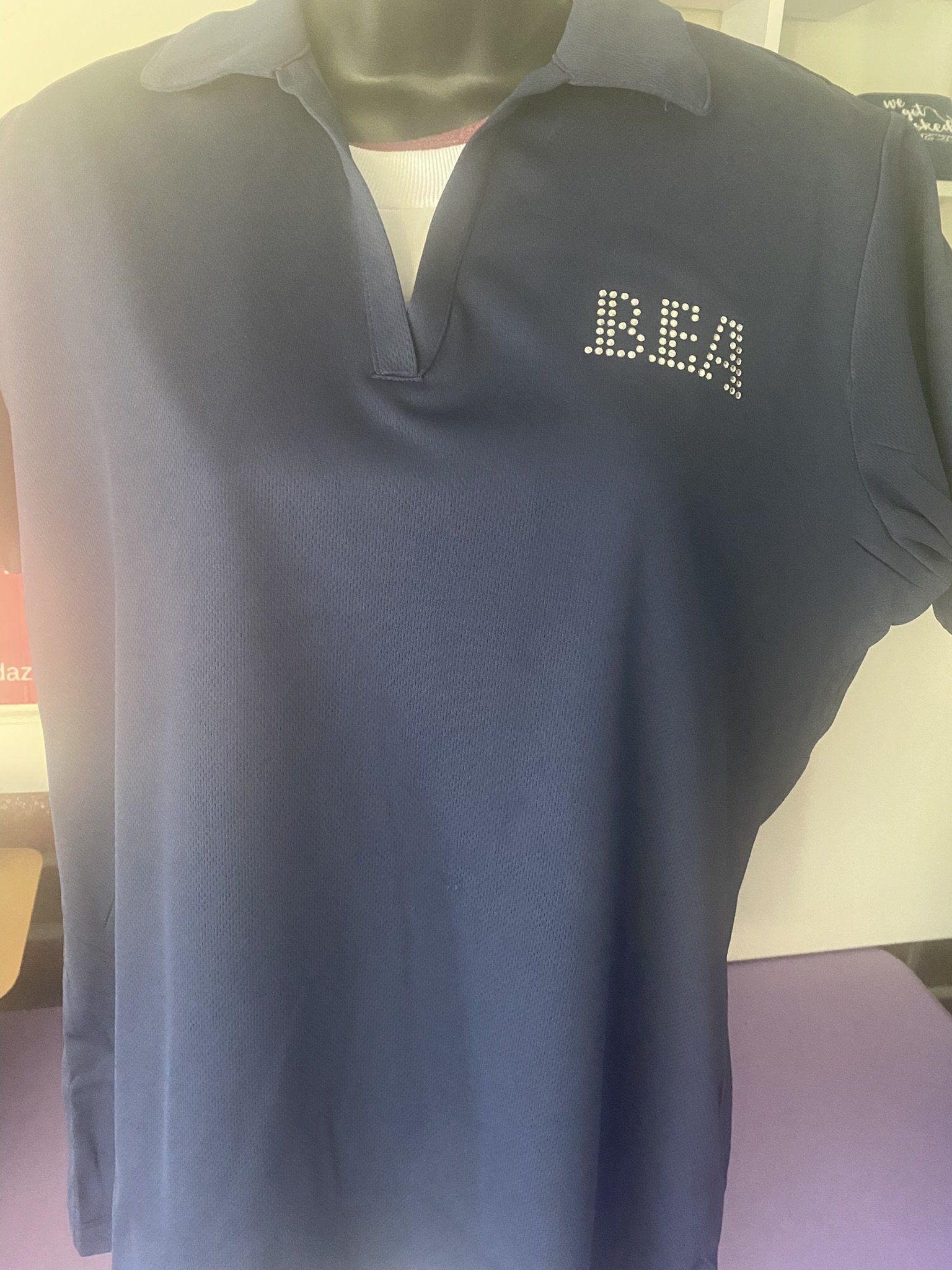 A black polo shirt with the word dea on it is on a mannequin.