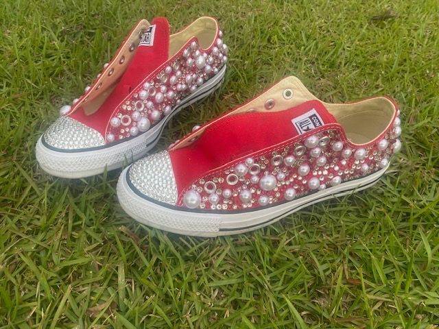 A pair of red converse shoes with pearls on them are sitting on top of a lush green field.