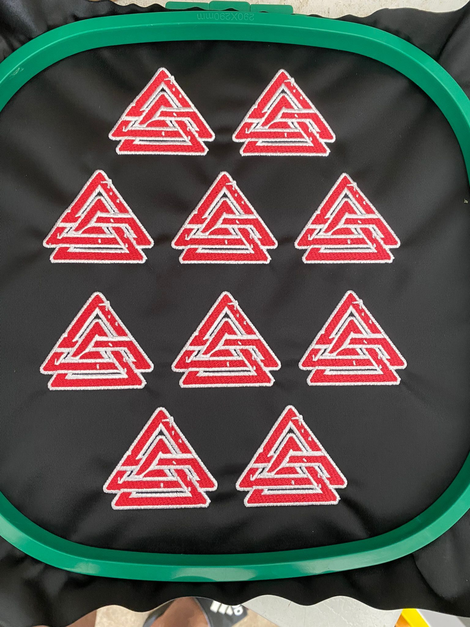 A green embroidery hoop filled with red and white triangles on a black cloth.