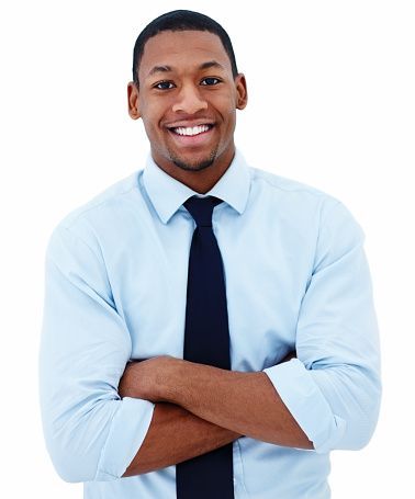 A man in a light blue shirt and black tie smiles with his arms crossed