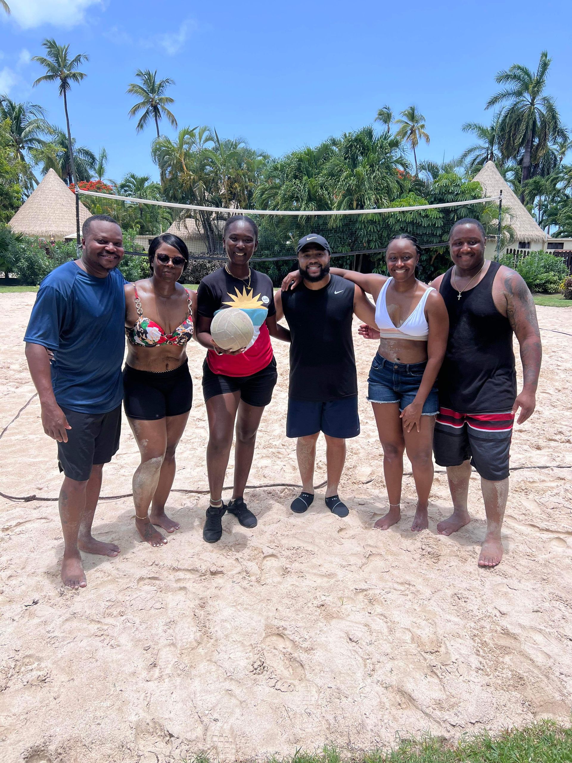 A group of people are posing for a picture on a beach volleyball court.