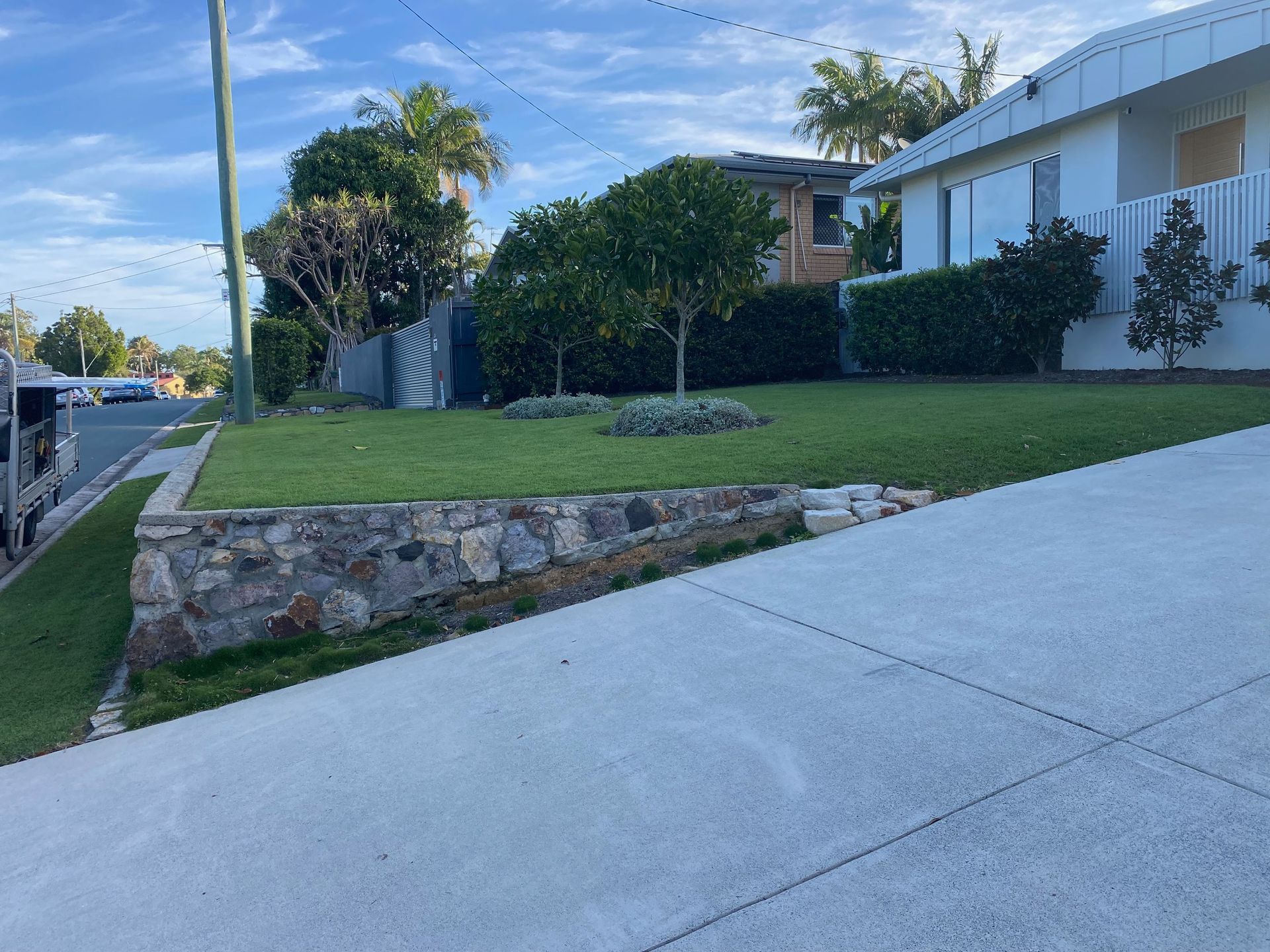 A lawn with a stone wall and a concrete driveway in front of a house.