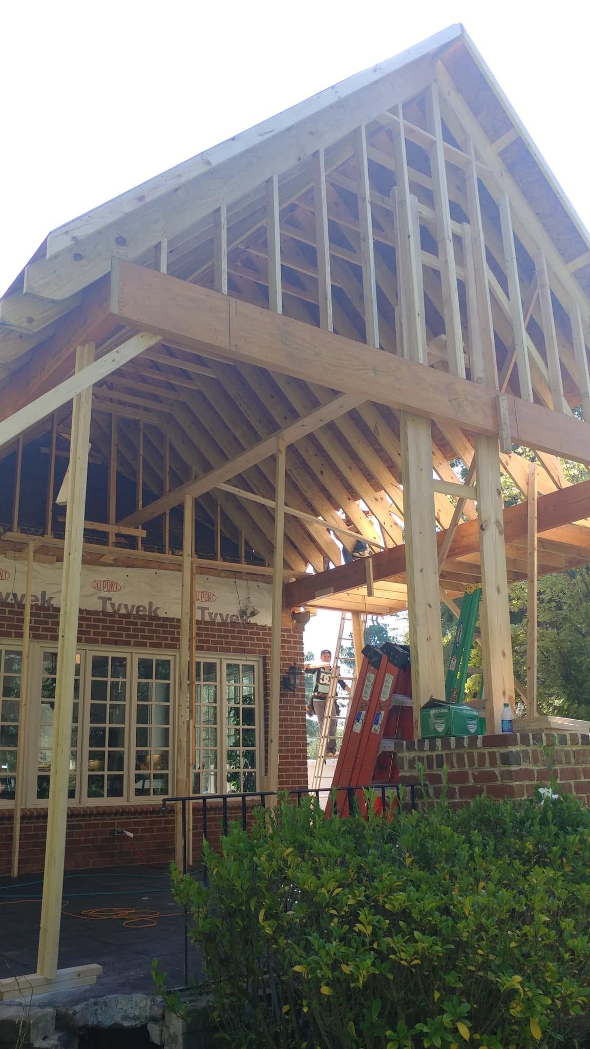 Outdoor wooden structure with a steep roof and exposed beams above glass doors and greenery