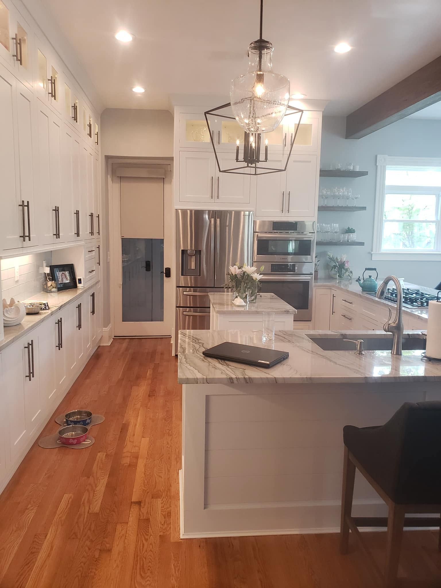 Bright modern kitchen with white cabinets, marble island, wood floors, and a stainless-steel fridge
