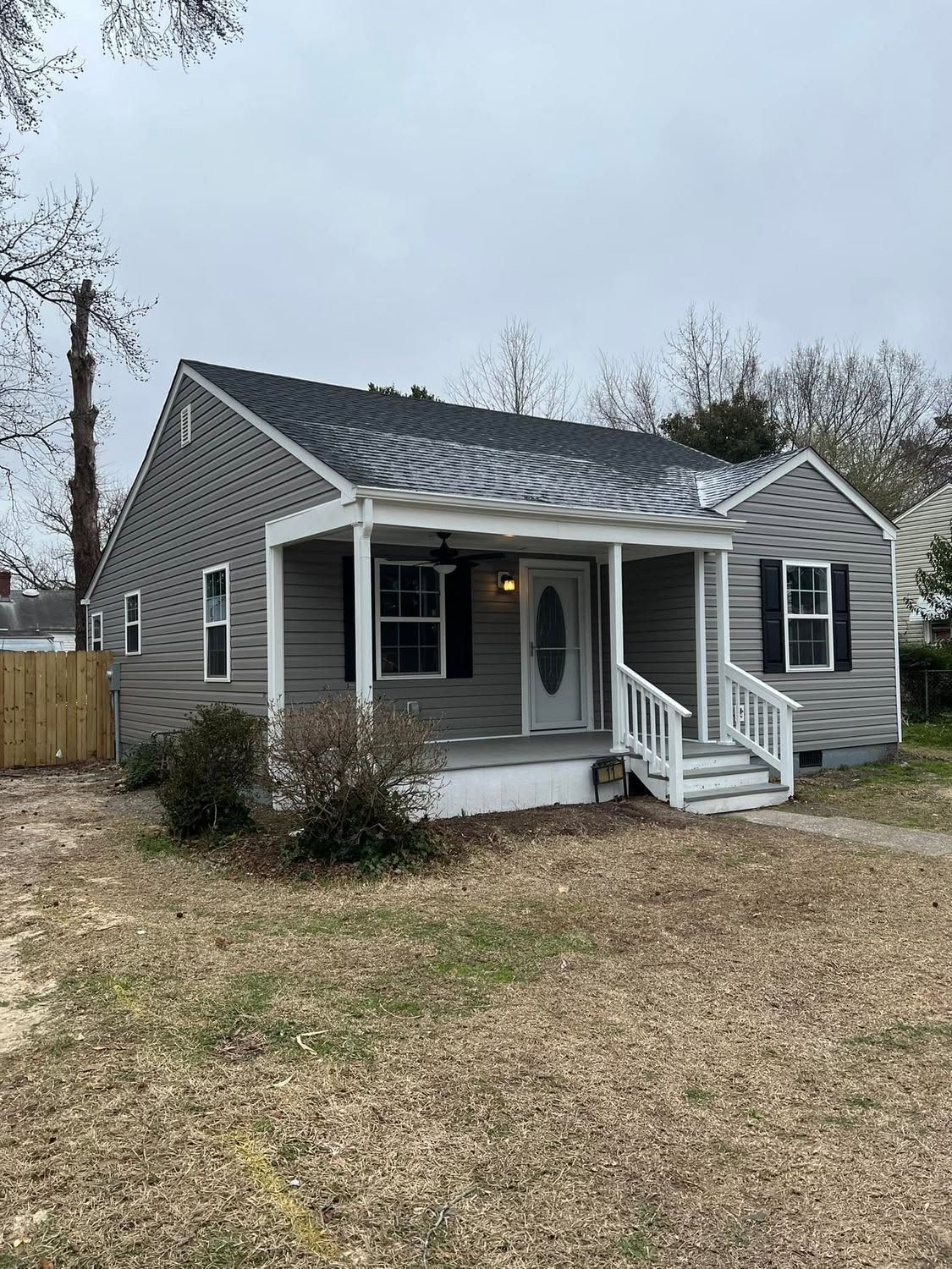 Gray cottage with white trim and porch, front steps, and a gravel yard under an overcast sky