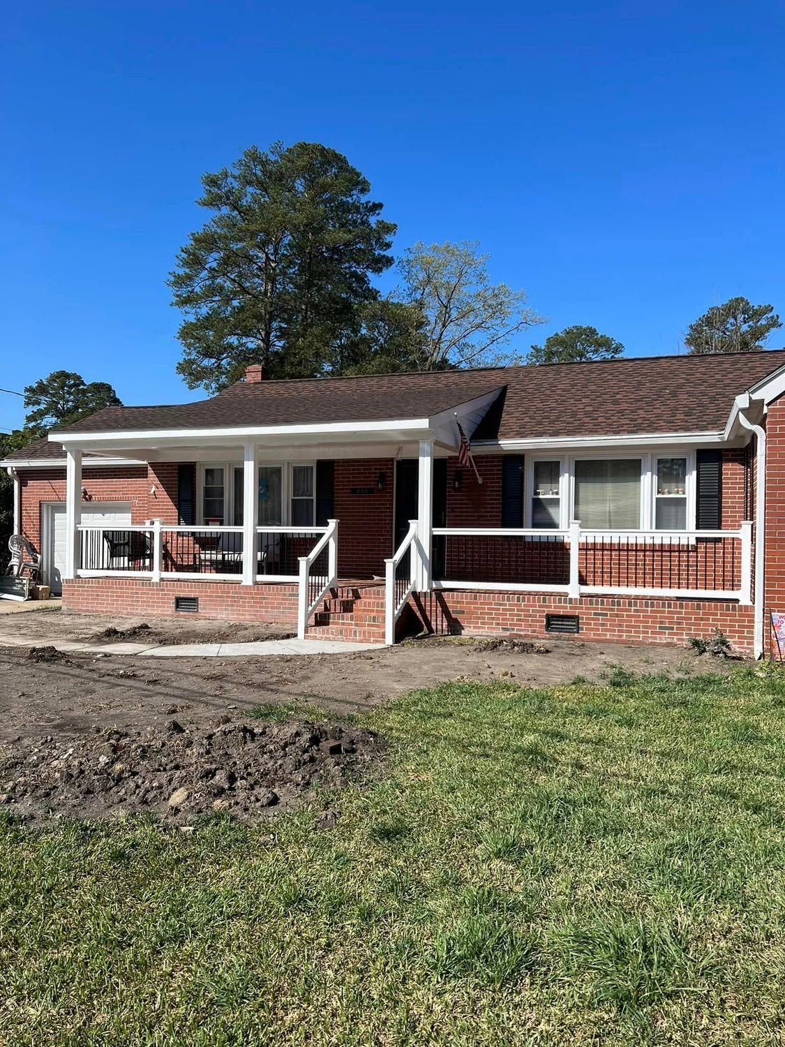 Single-story brick house under renovation with front porch, exposed framing, and dirt yard under a blue sky