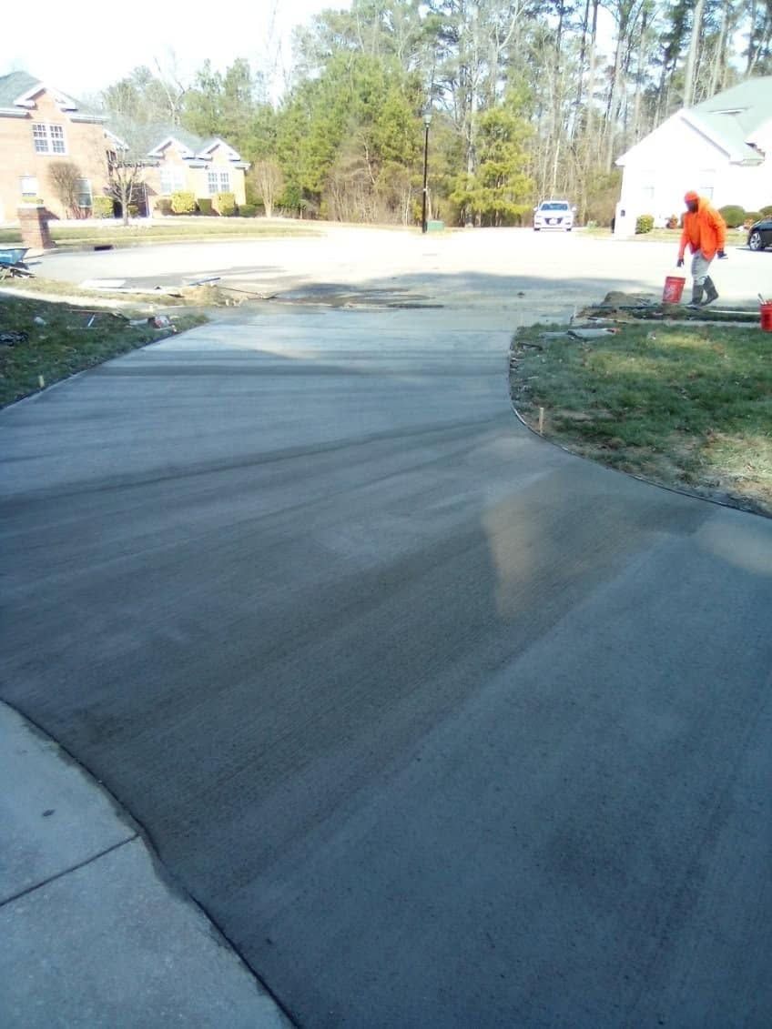 Freshly poured concrete driveway beside a house, with a worker in orange on the right.
