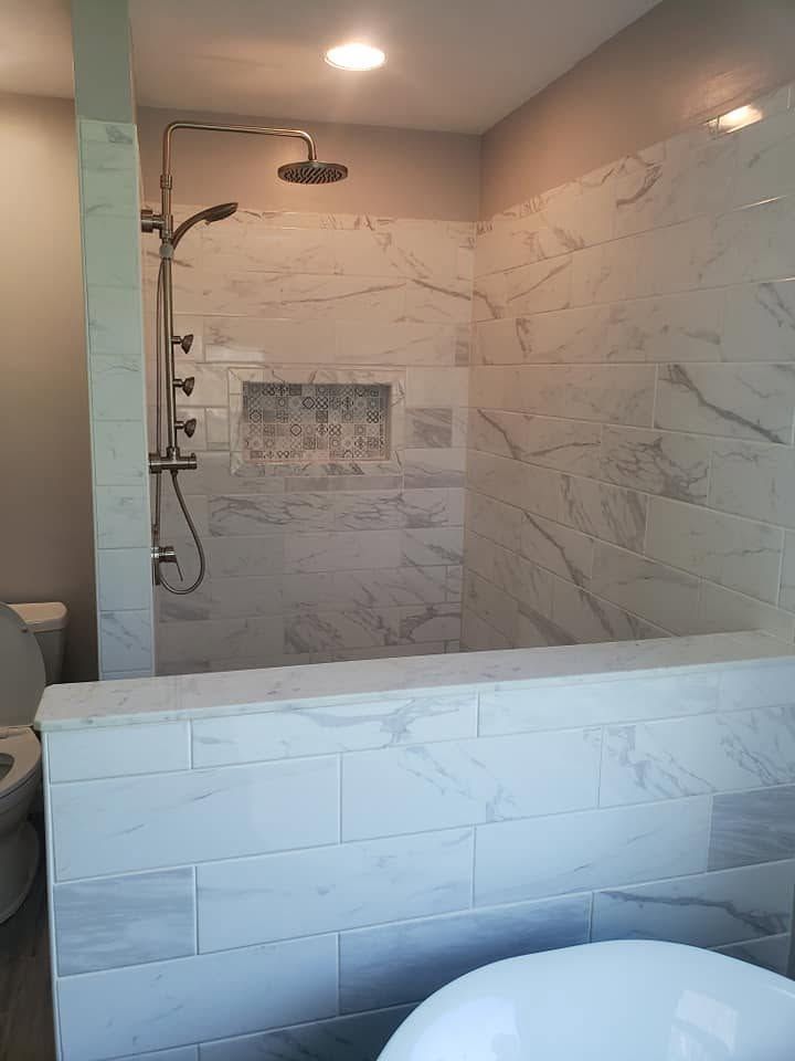 Modern bathroom with marble-look shower, glass partition, and white bathtub ledge