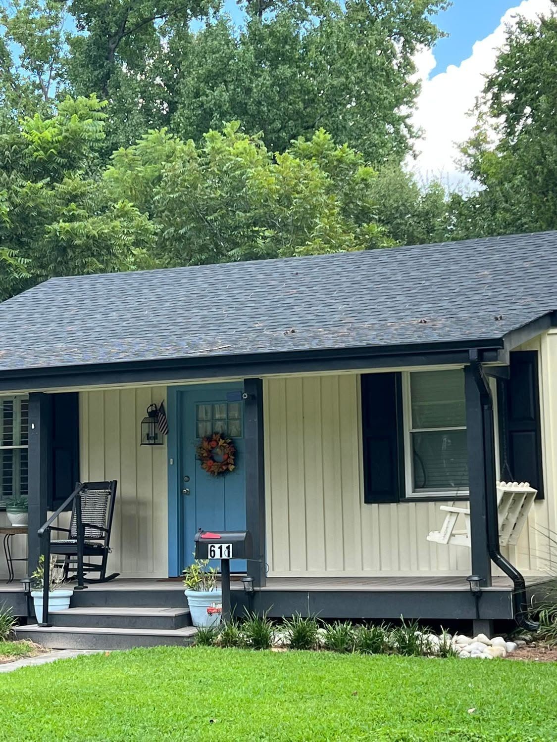 Single-story house with gray roof, blue front door, and a small porch surrounded by greenery